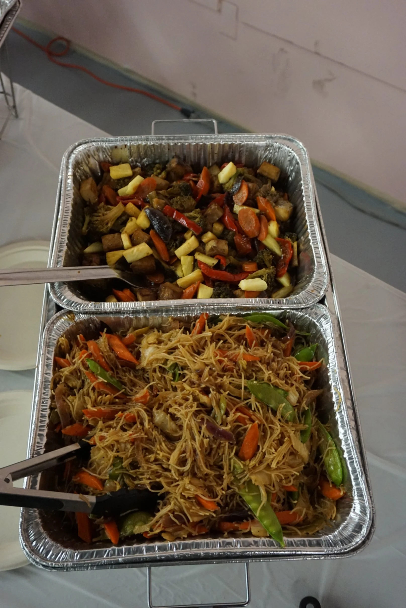  Pancit and vegetables in tin tray with serving utensils on table 