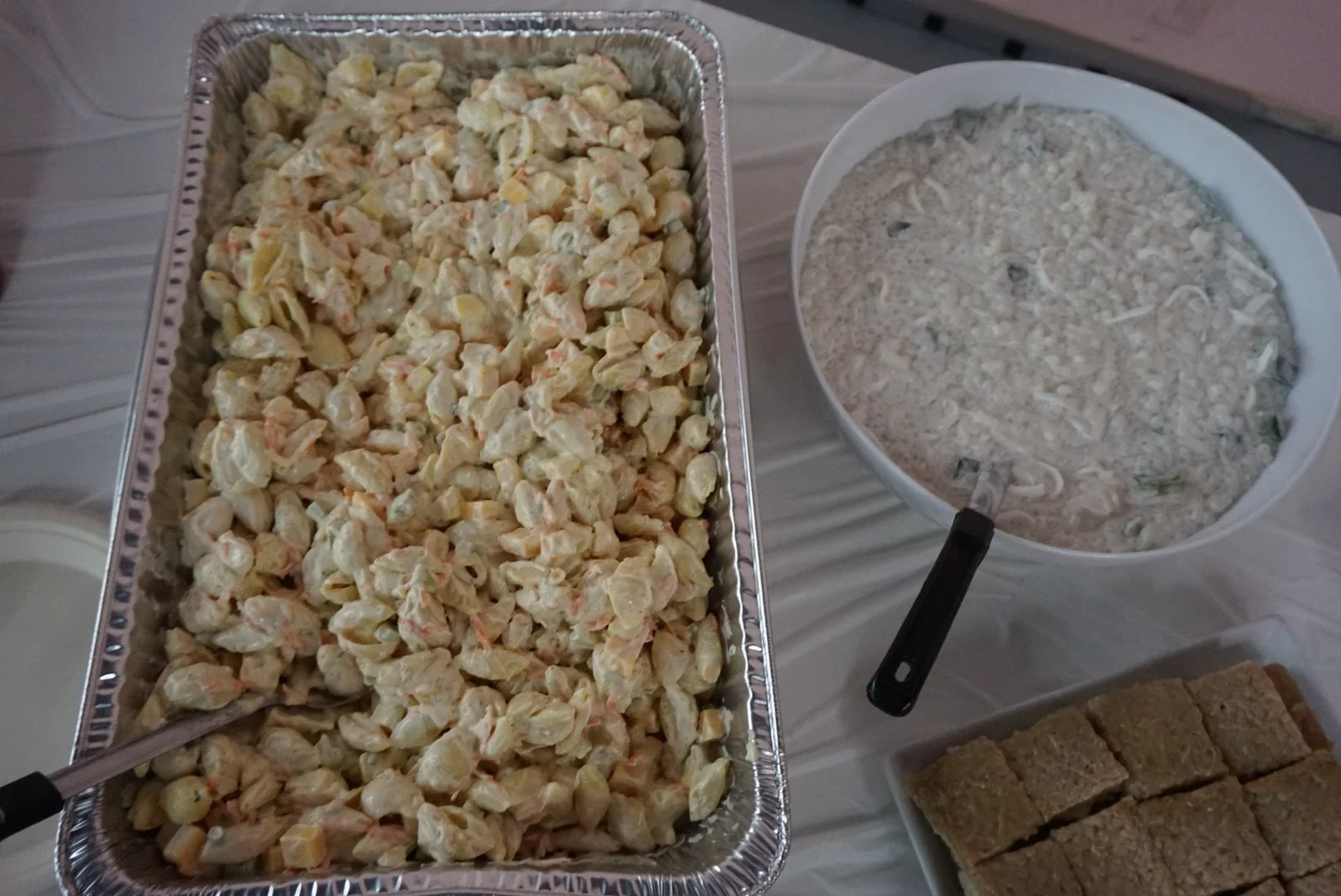  Large tray of macaroni salad on the left with white bowl of buko pandan on right, below a tray of biko 