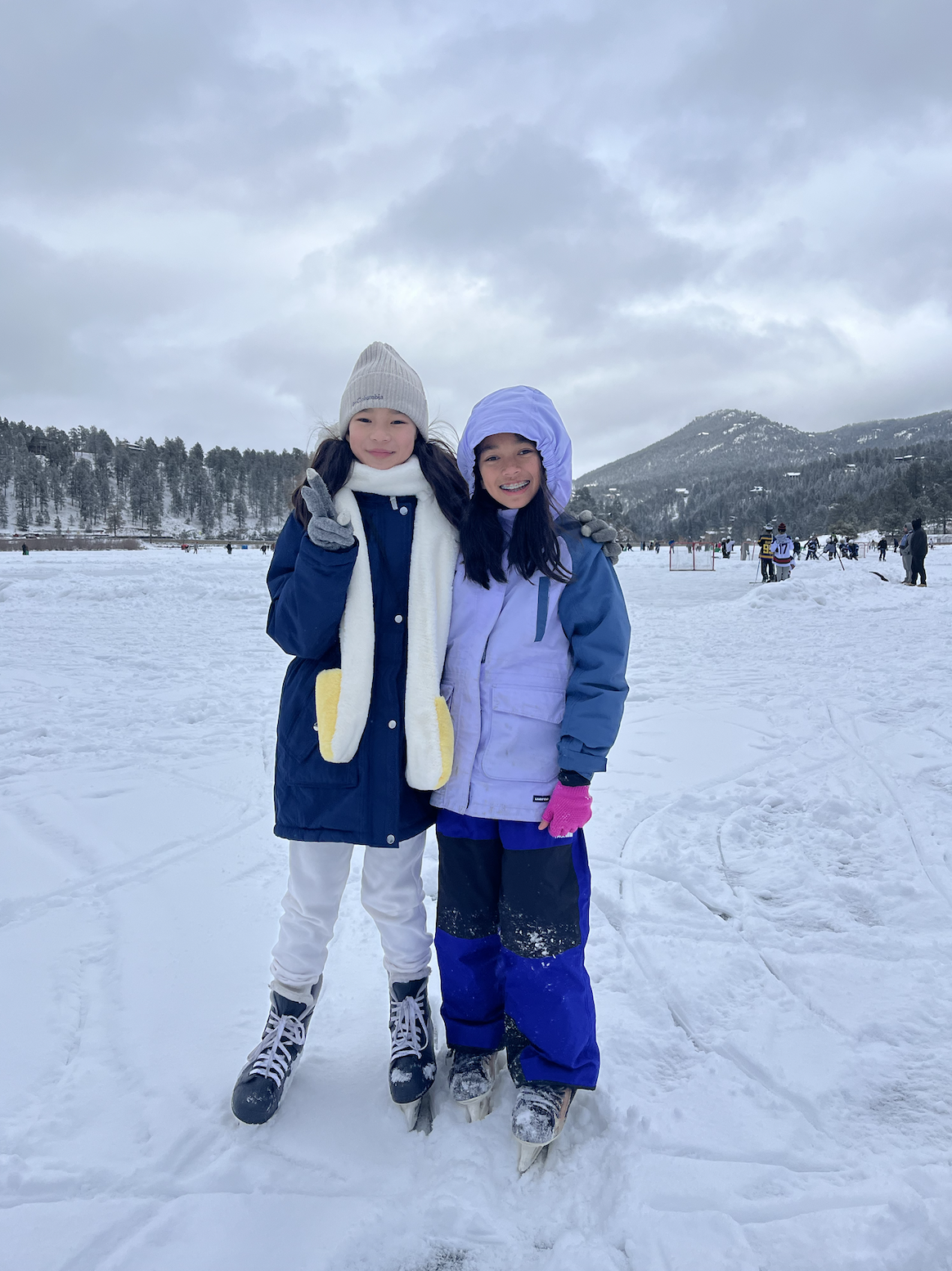 two asian american girls smiling on ice with skates with the beautiful colorado mountains behind them