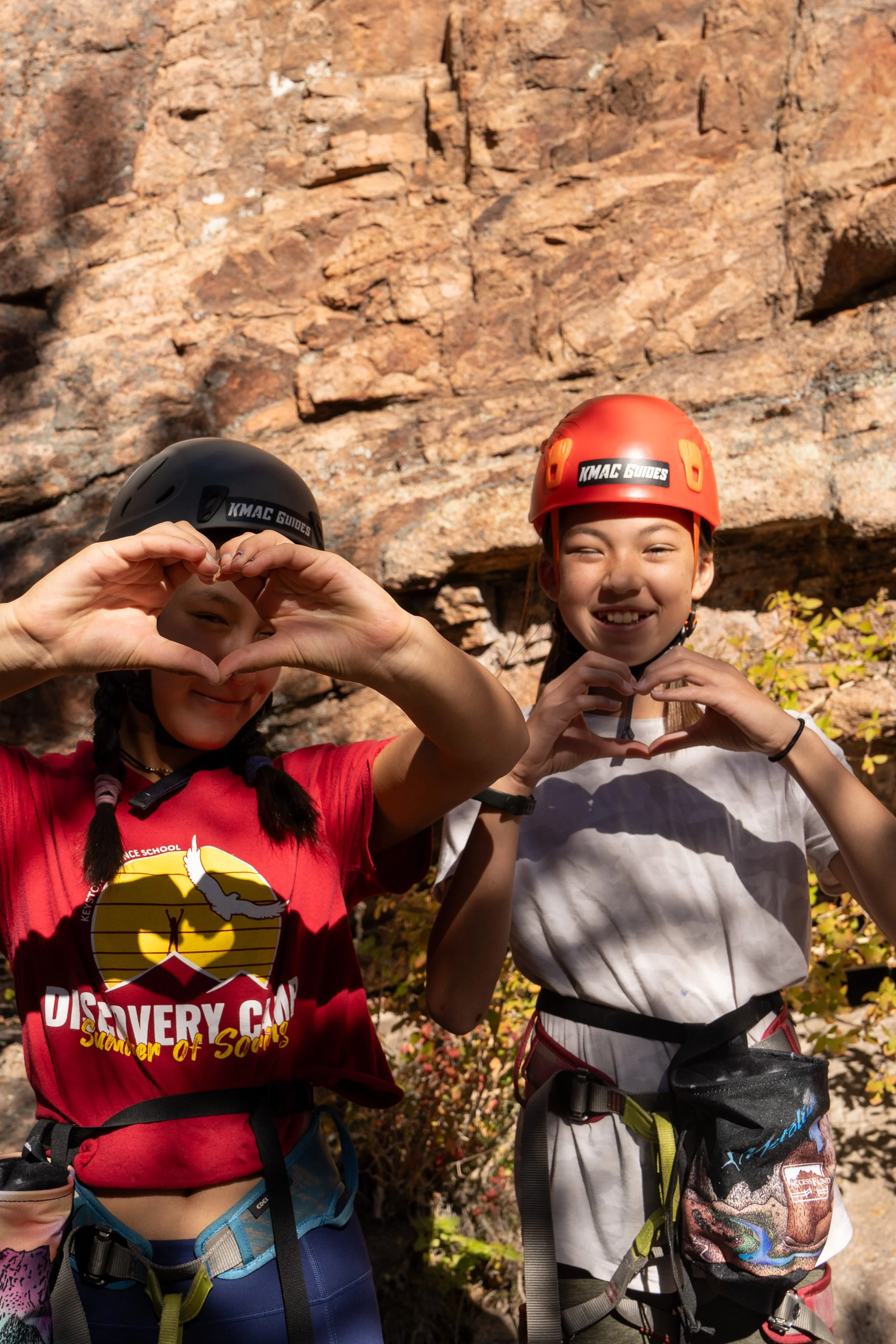2 asian american girls during rock climbing event in colorado doing hand hearts