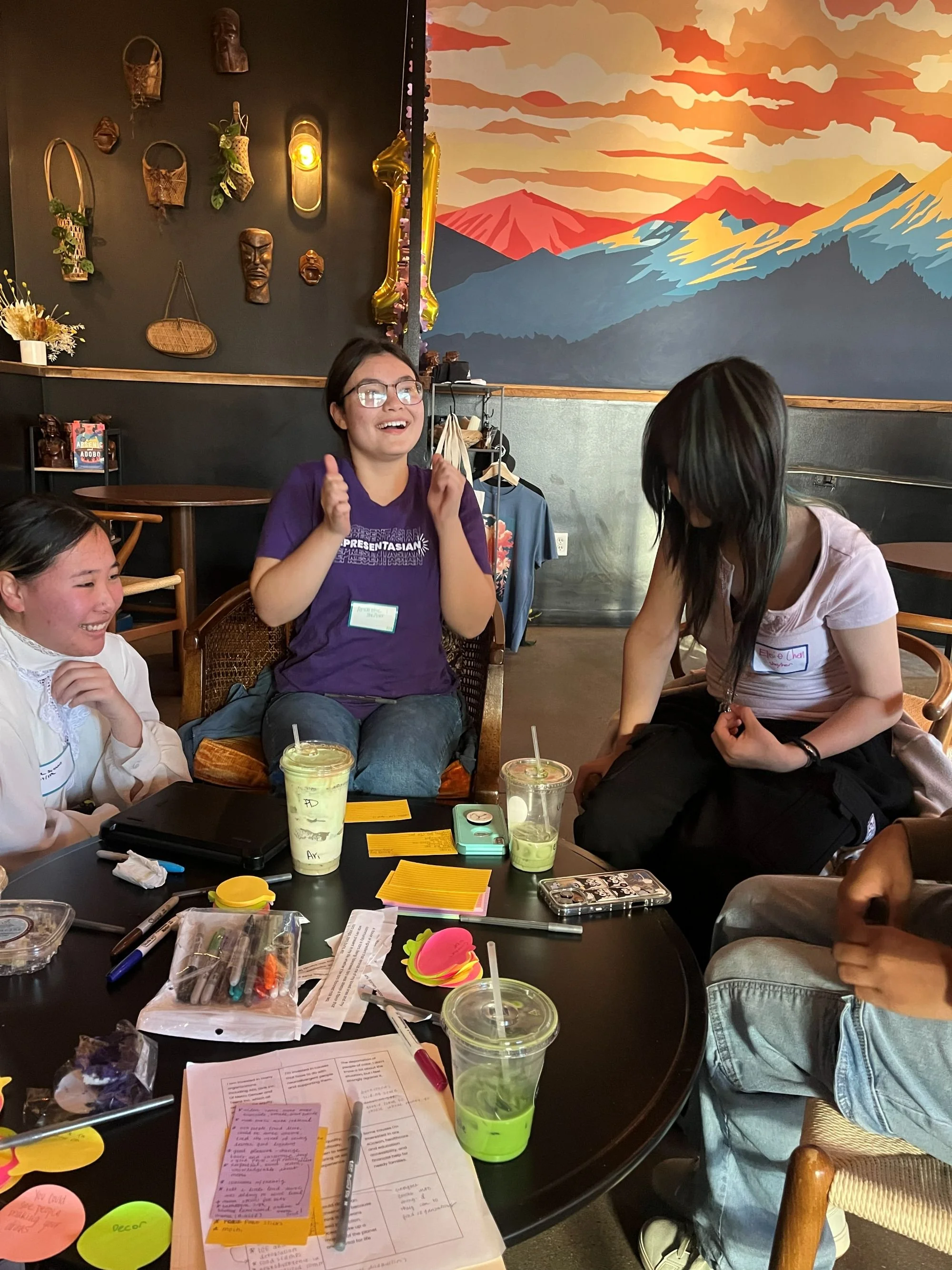  Three students sitting separately and all talking together to brainstorm with a table of post-its and drinks.  