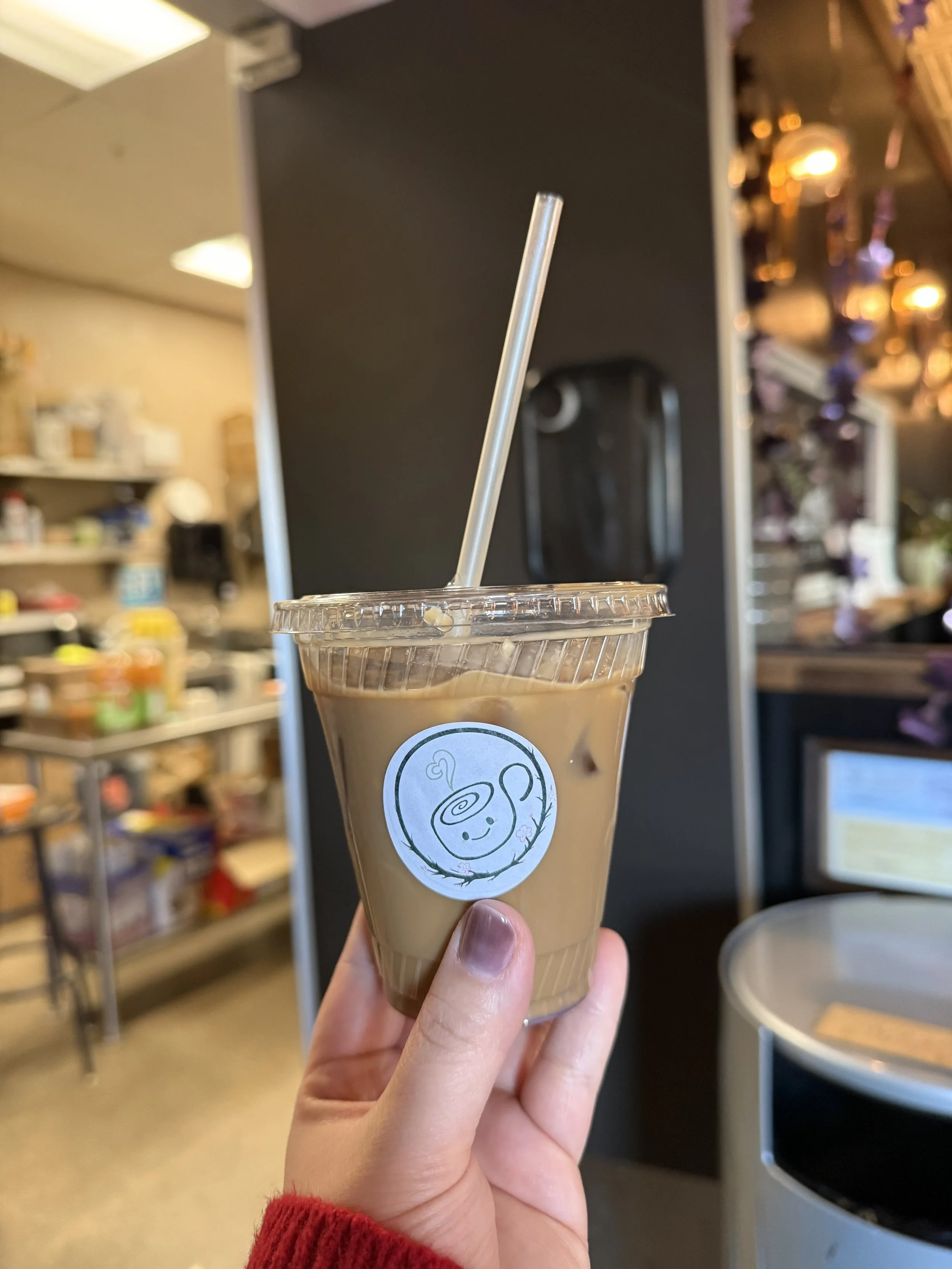  Hand holding the Purple Mountain Ube drink in a plastic cup with a straw. Cafe for a Day logo on a white sticker. 