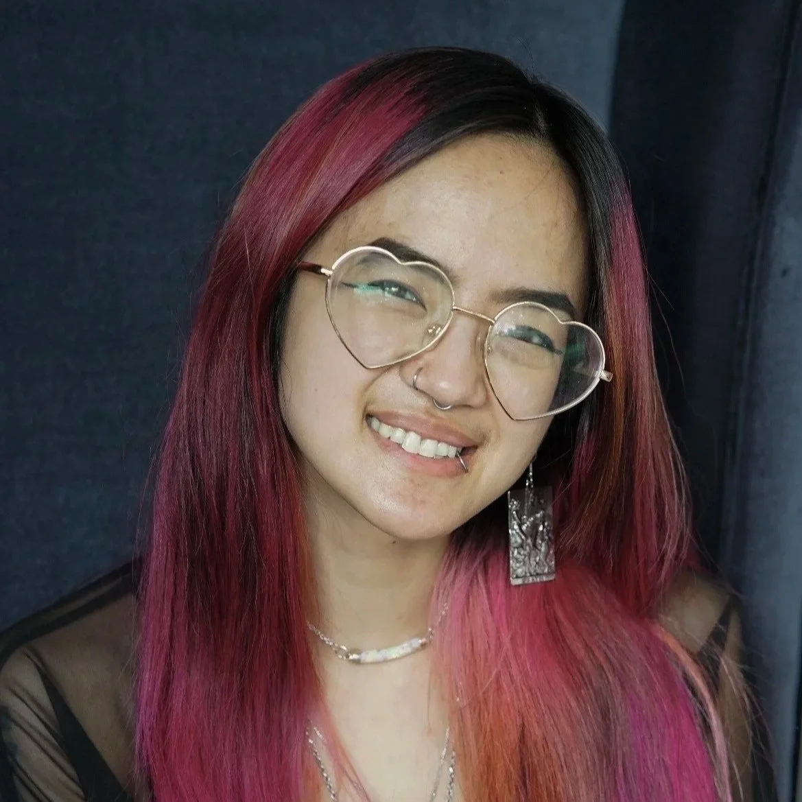asian american audio engineer with red/pink hair and heart shaped glasses smiling