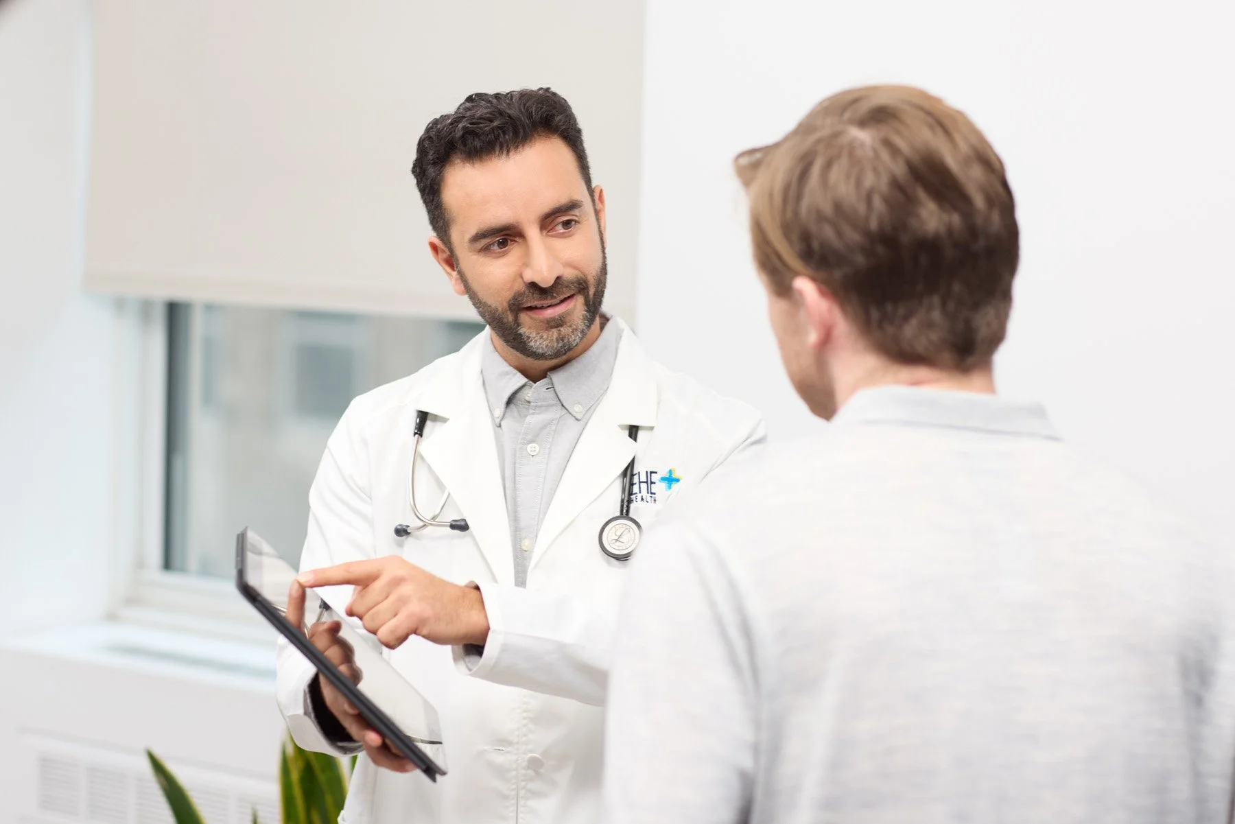 Physician consulting with patient using tablet, medical office portrait photography