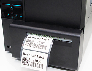 Thermal transfer printer printing heatproof barcode labels with QR codes, barcodes, and product identification text.