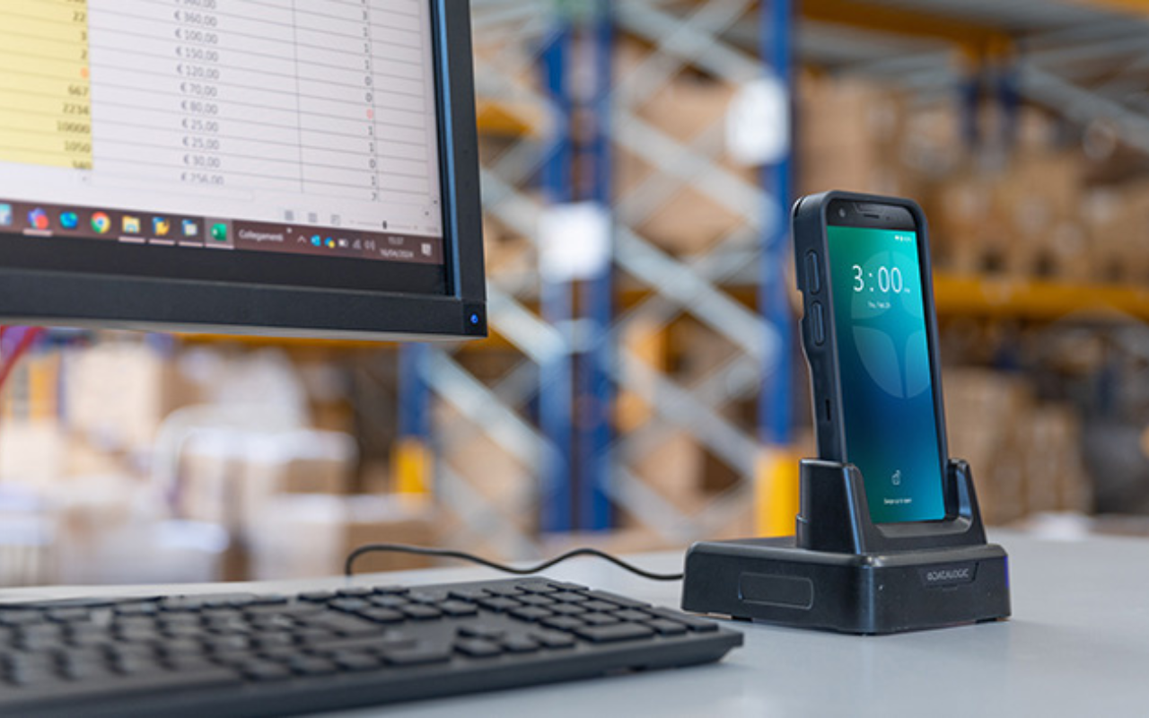 mobile computer on a desk with a warehouse in the background and a computer to the left