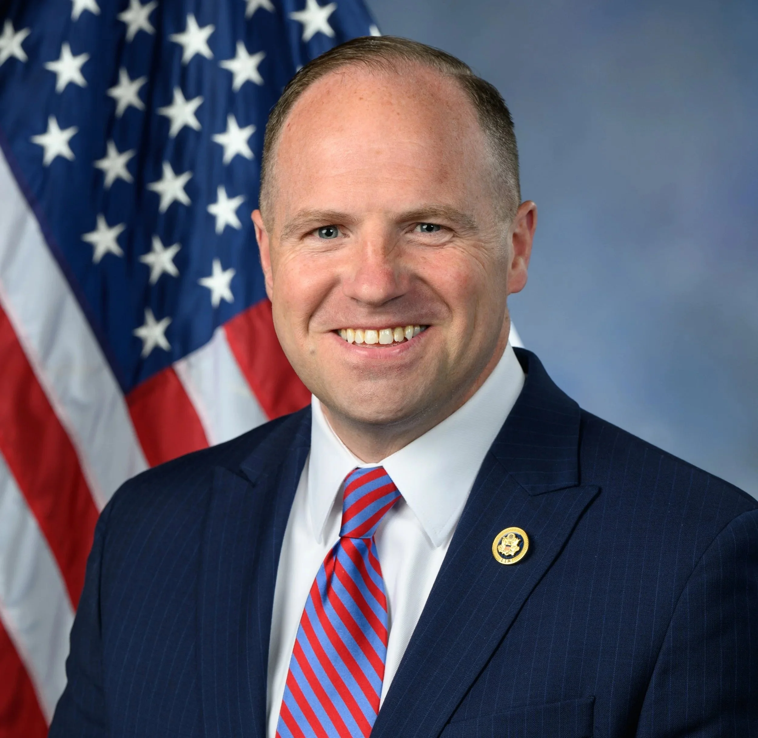 Portrait of a man in a suit with an American flag in the background.