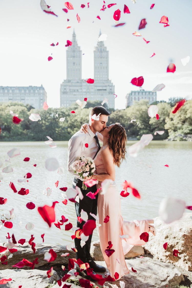 Couple kissing beside the Central Park lake in a shower of rose petals