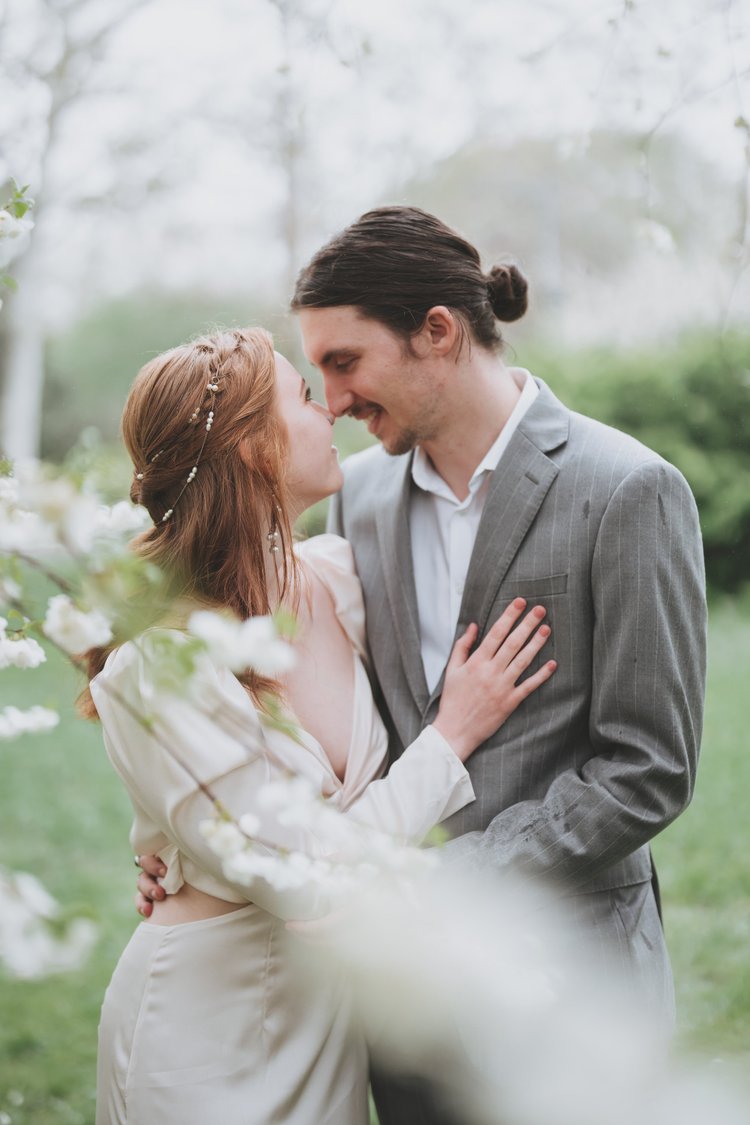 Couple foreheads together behind branches of white spring blossom