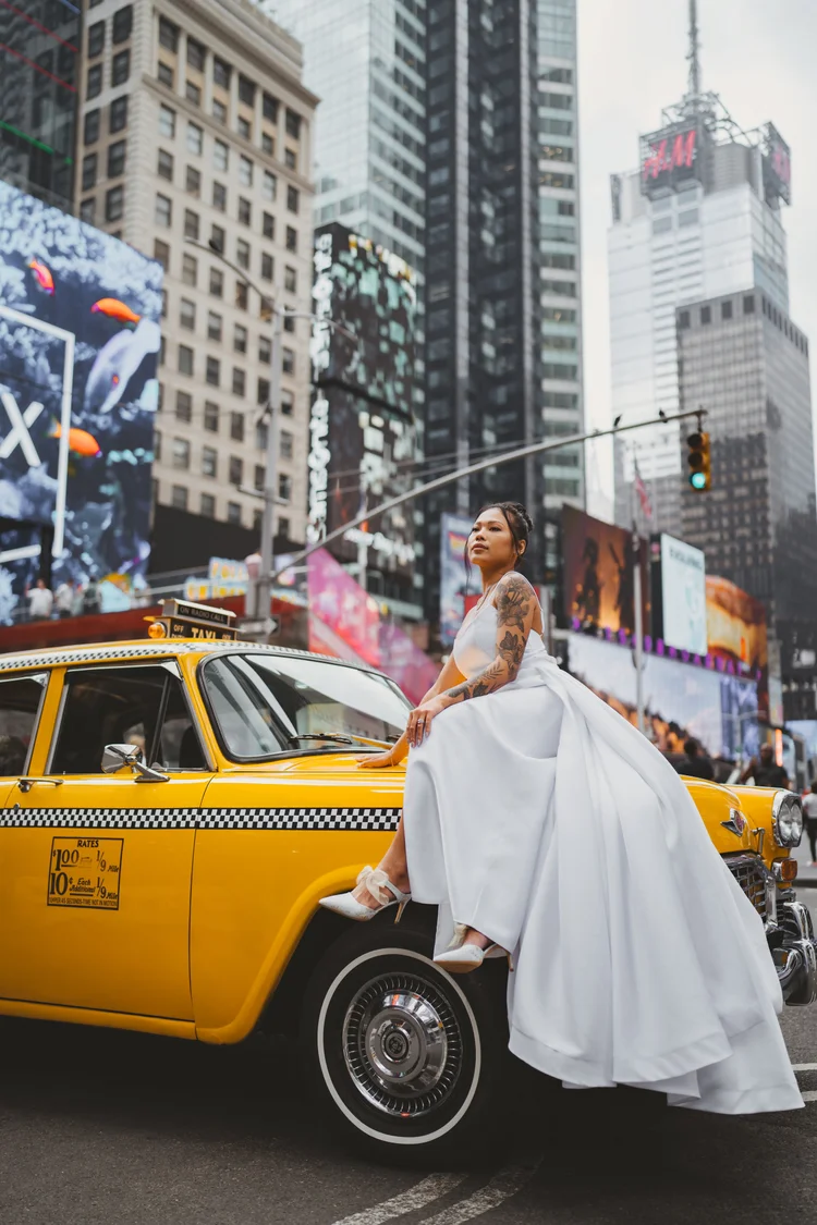 Bride in a long train leaning against a yellow taxi in Midtown