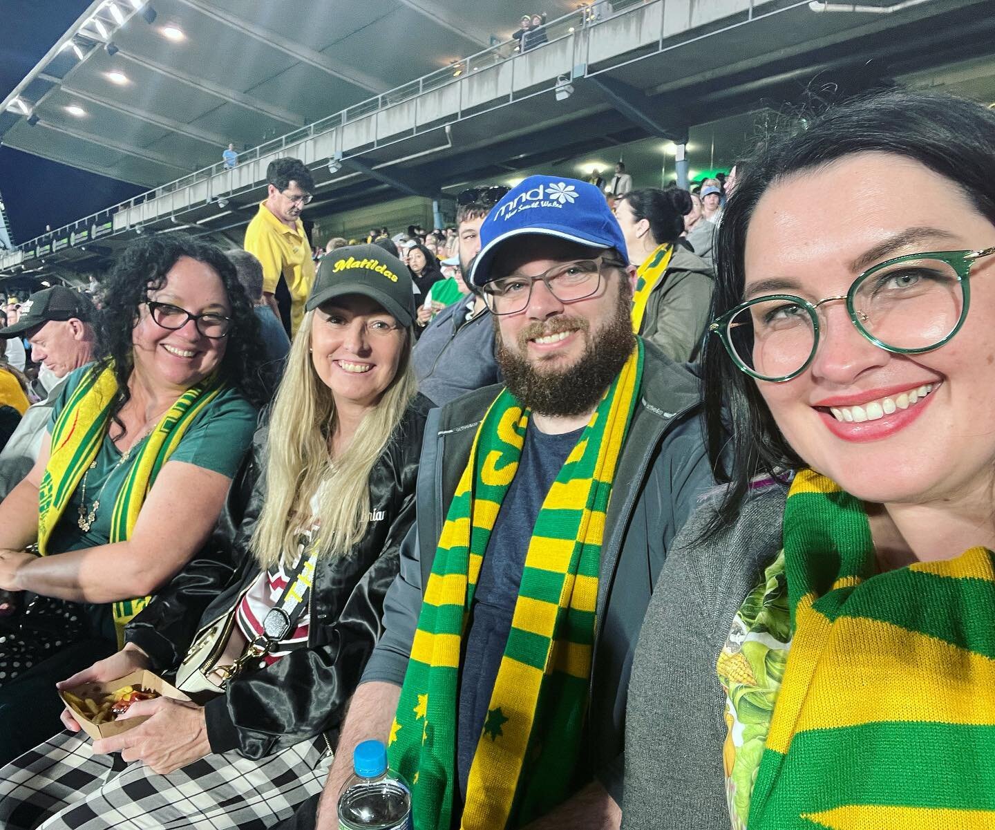 #matildas with the bay 4 crew 

Image: 4 smiling humans in green and gold get up sitting in a football stadium.
