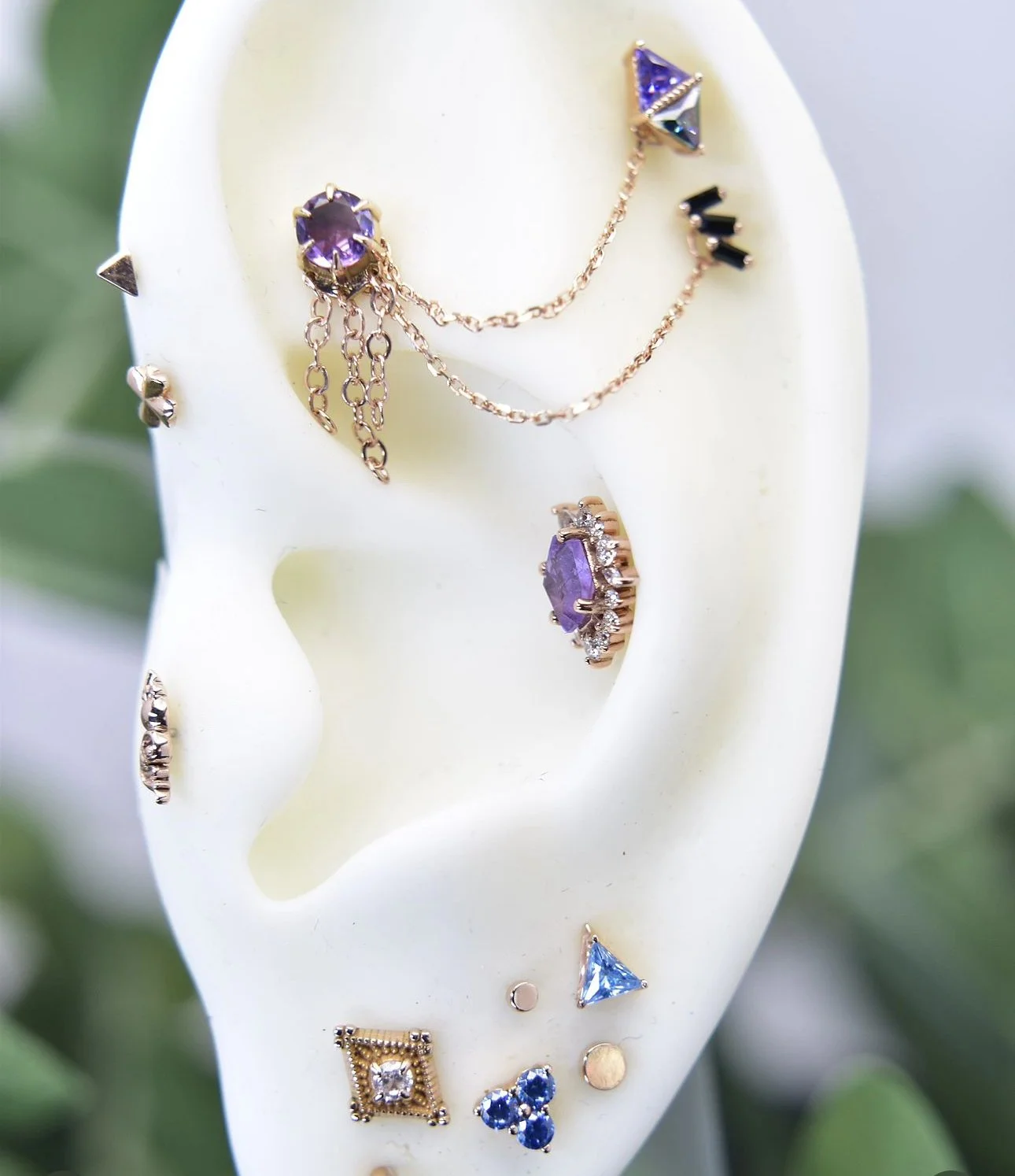 Multiple earrings with purple and blue gemstones on a white jewelry display ear.