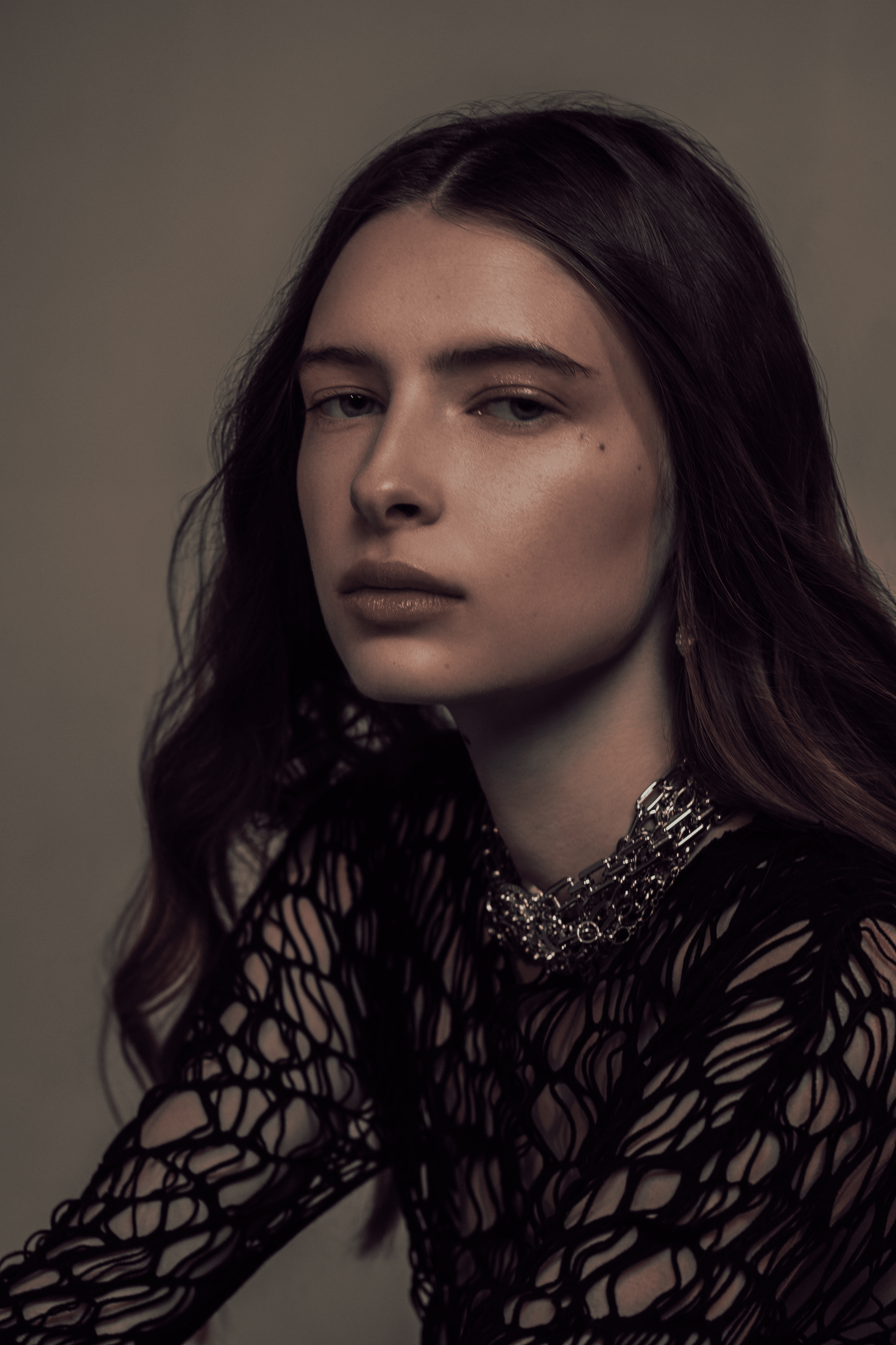 Close-up portrait of a woman with dark hair wearing a black, open-knit garment and a layered silver necklace.