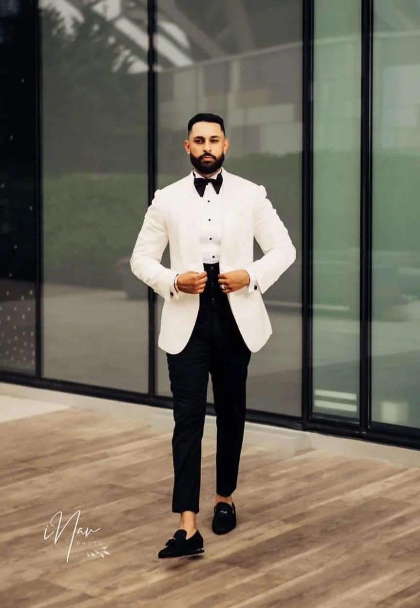 A groom in an ivory dinner jacket and black trousers by Modello Bespoke