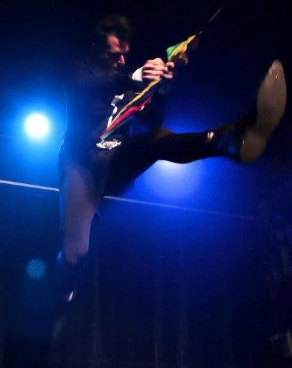 Performer on stage playing electric guitar in a low-angle shot with blue stage lighting.