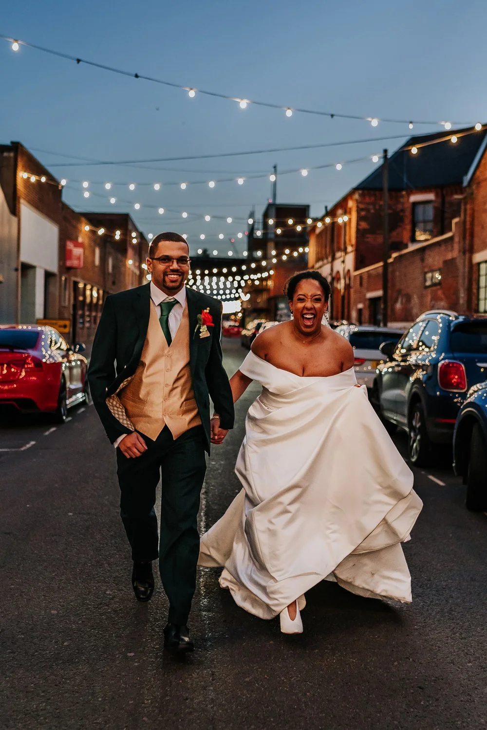 Couple running and laughing down an urban street in Birmingham on their wedding day