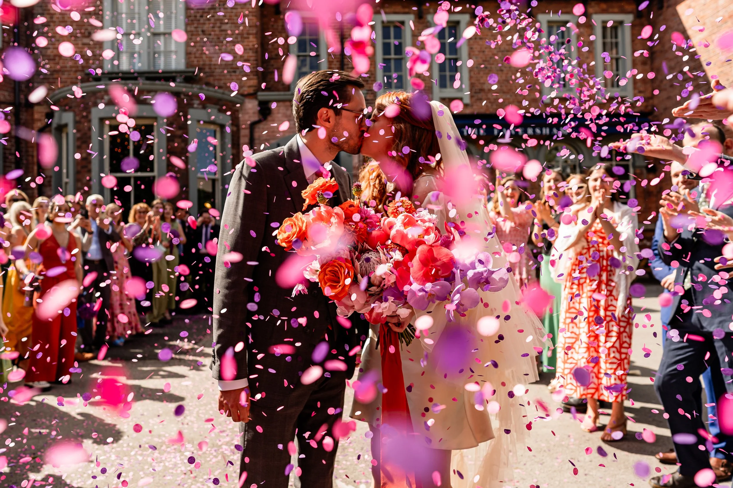 Bride and groom kissing under colourful confetti outside Leeds wedding venue