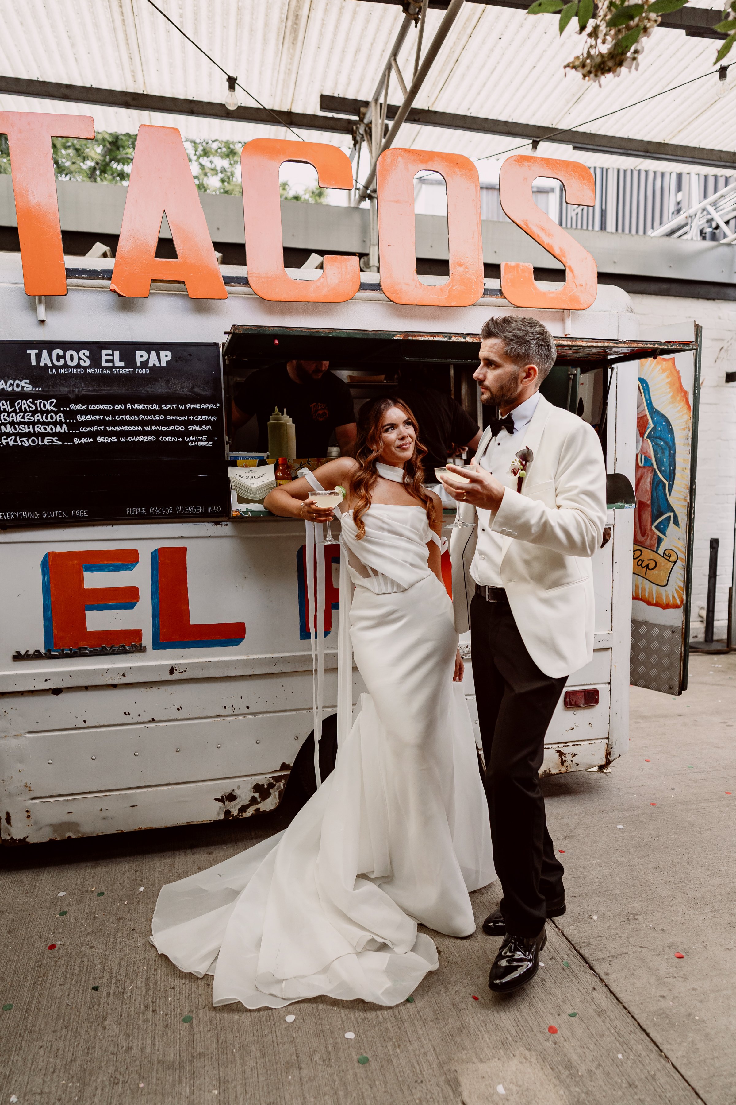 Bride and groom with their cocktails outside a taco truck on their non traditional wedding day