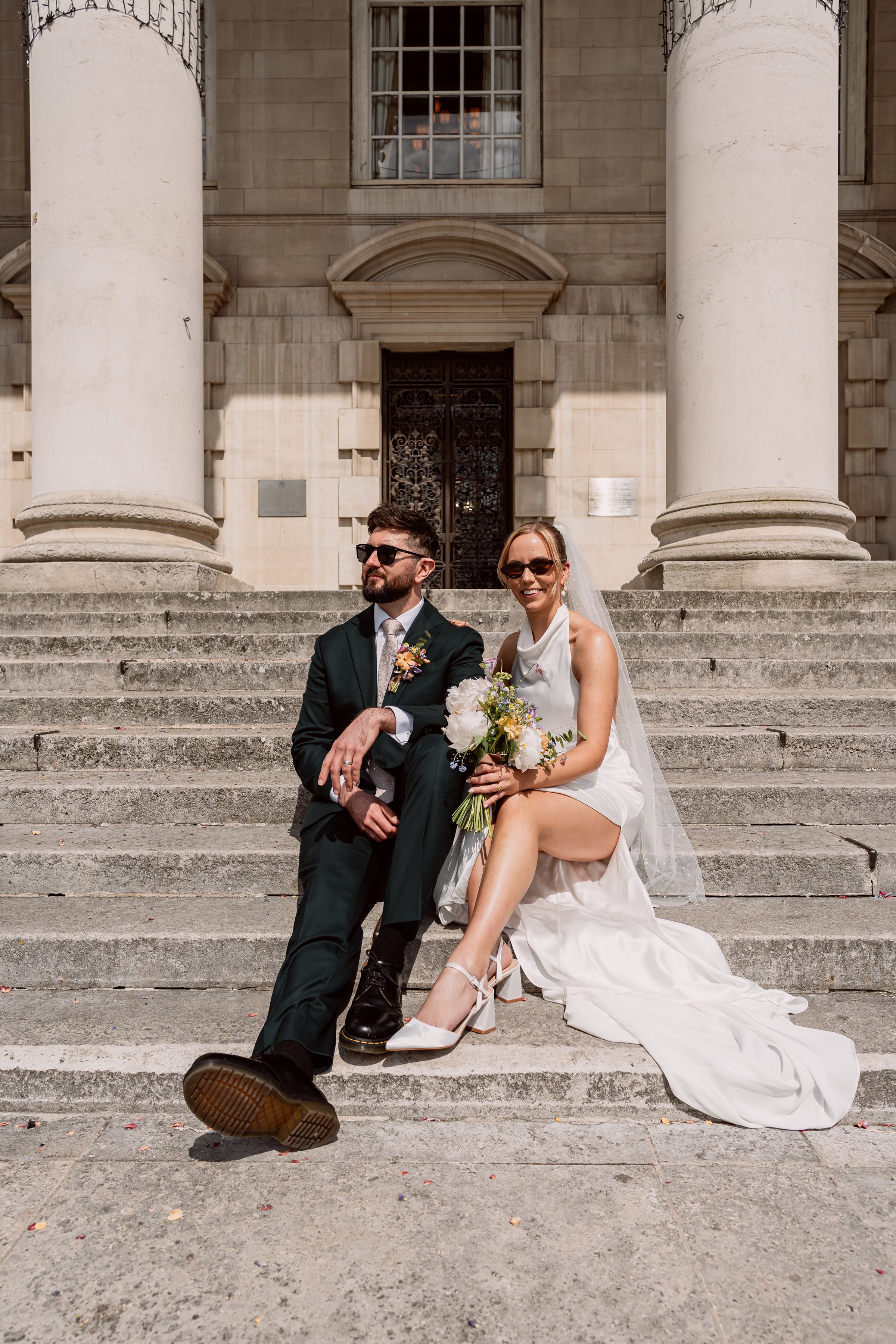 Bride and groom sitting on steps outside Leeds Town Hall on their wedding day