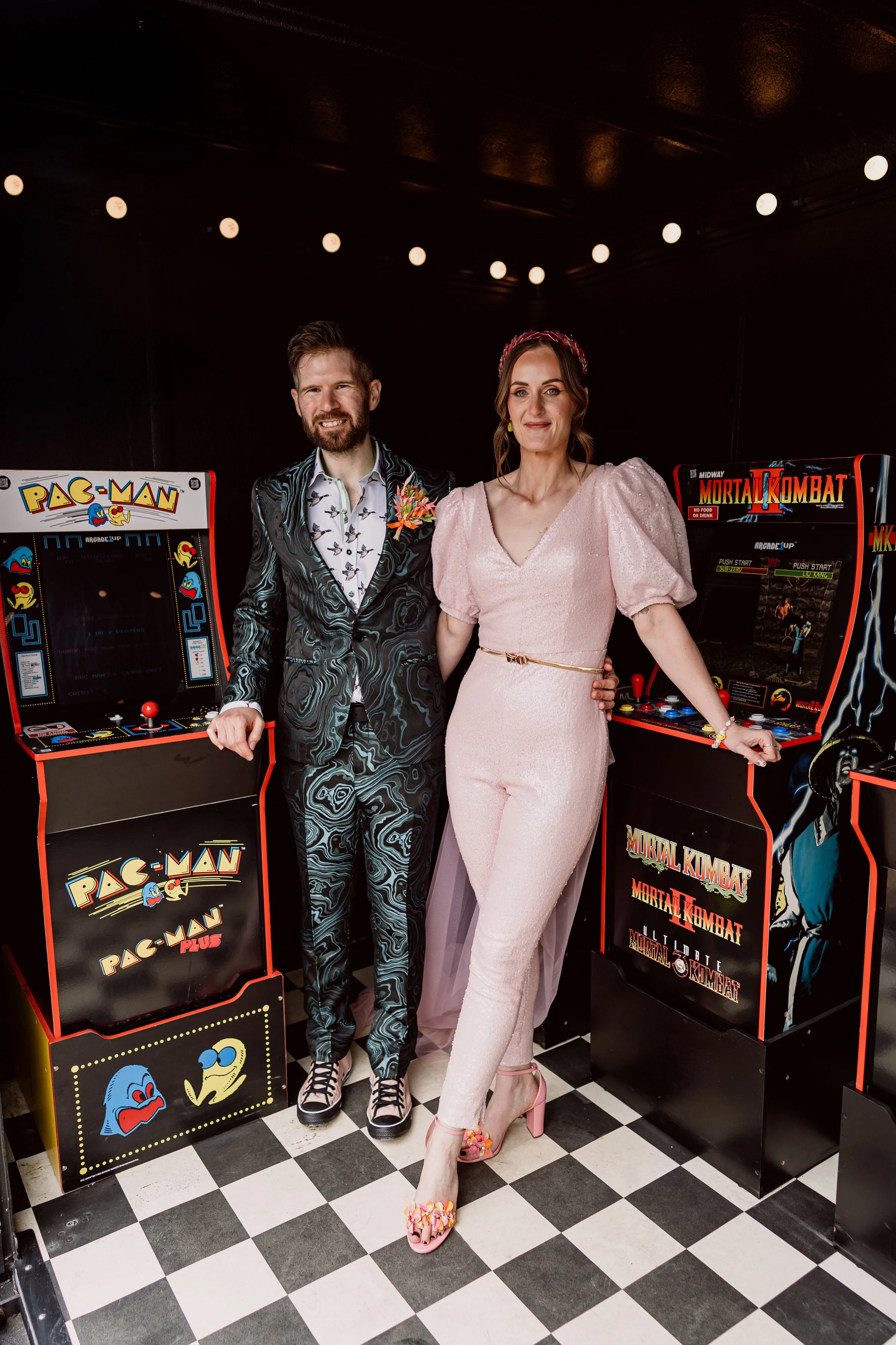 The bride and groom posing in front of retro arcade machines at their non-traditional wedding