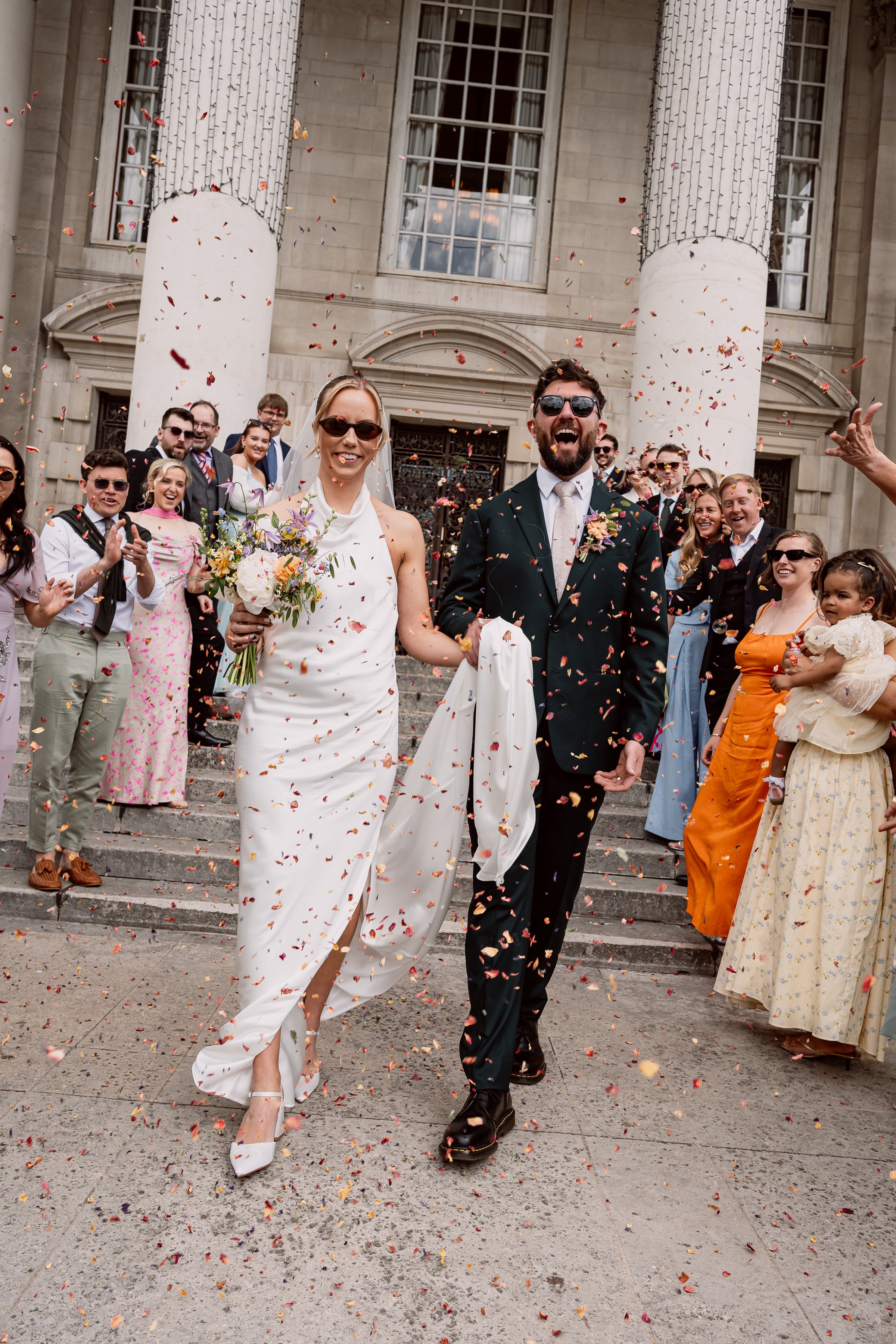 Bride and groom smiling as they walk through confetti on their wedding day in Leeds