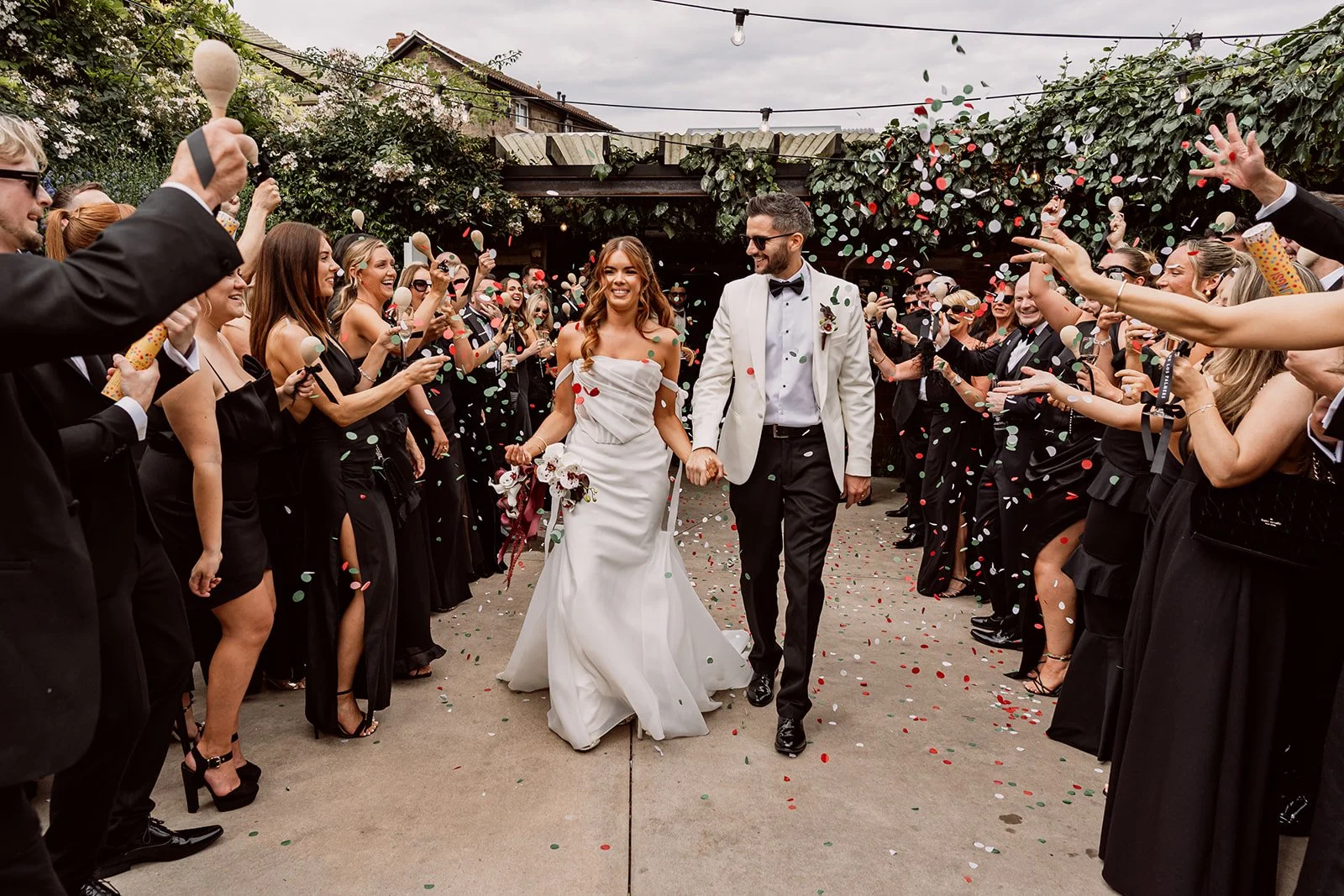 Couple holding hands walking through guests as they throw confetti at Birmingham wedding