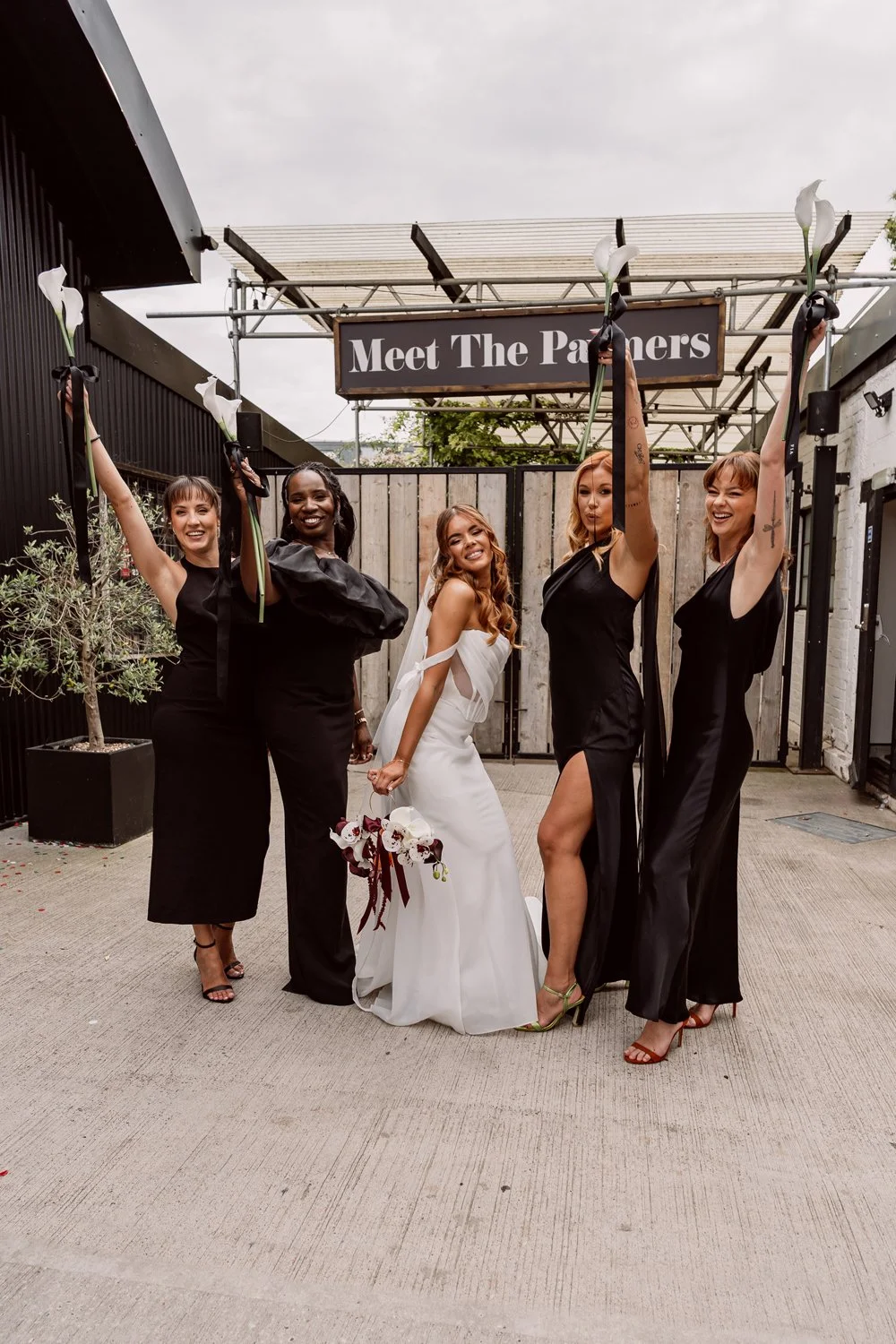 bride and bridesmaids holding flowers in the air outside alternative wedding venue
