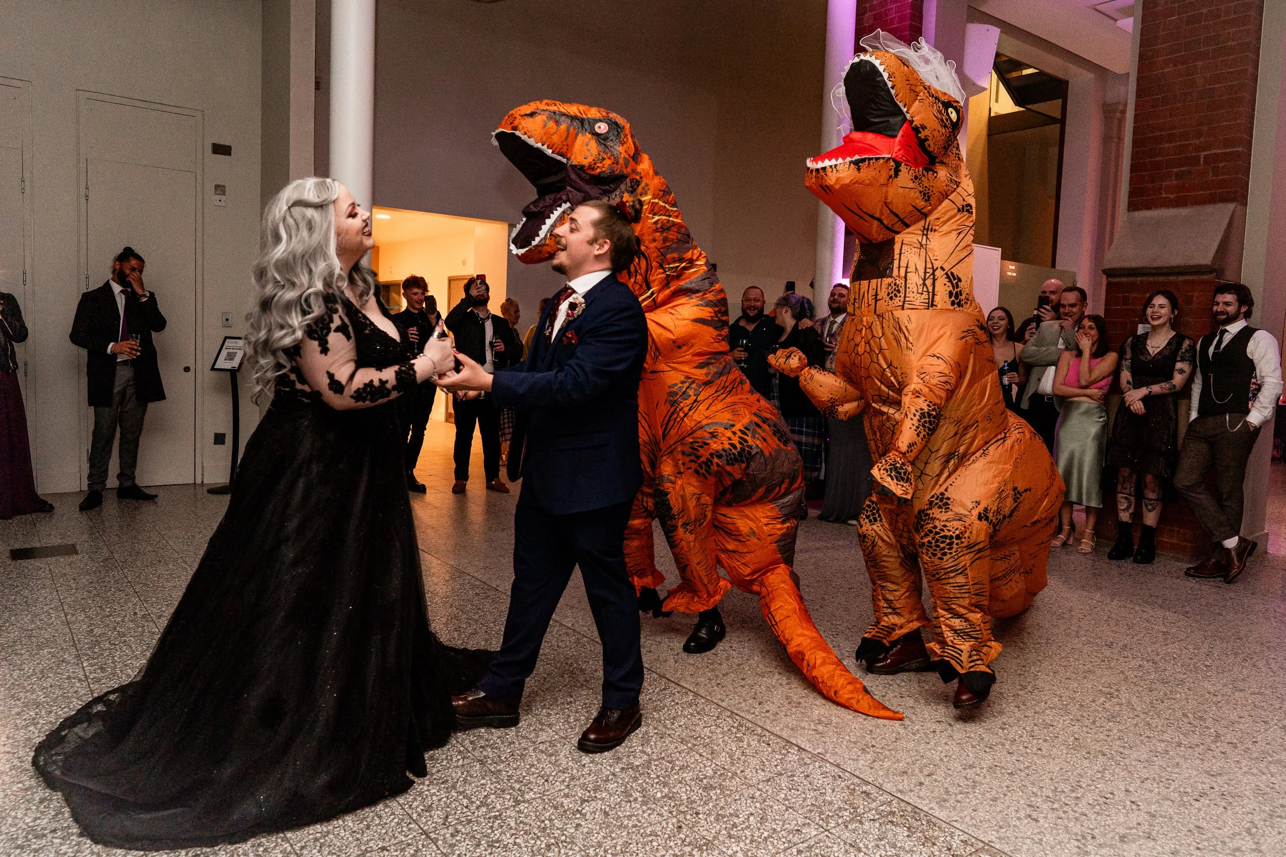 A couple standing with two dress up dinosaurs at their city wedding in Manchester museum