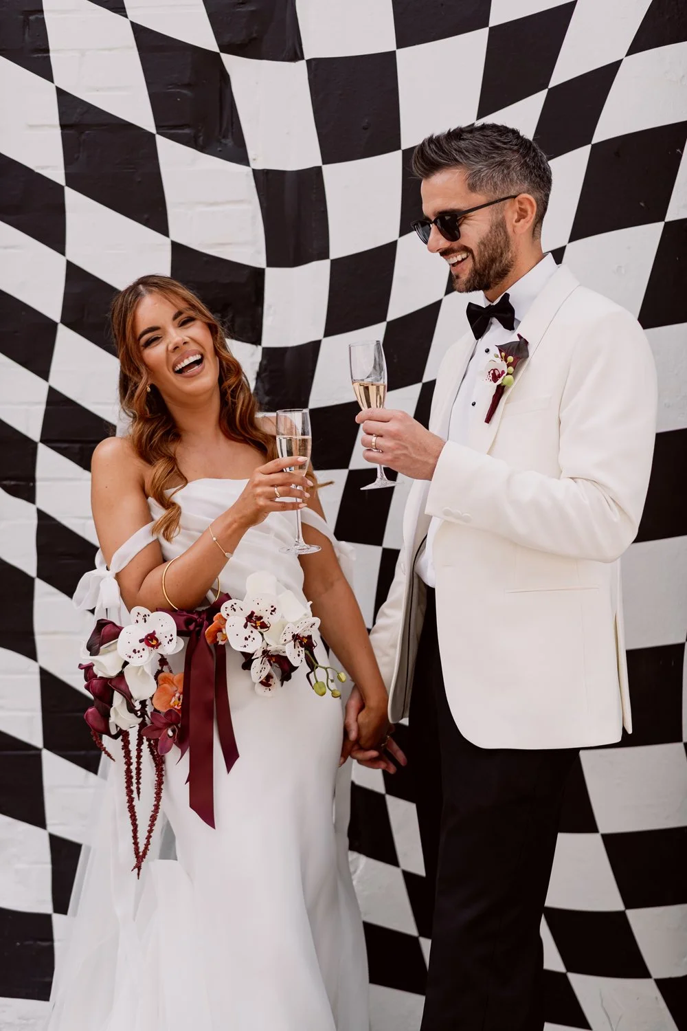 Bride and groom laughing in front of checkerboard graffiti at alternative Hereford wedding venue