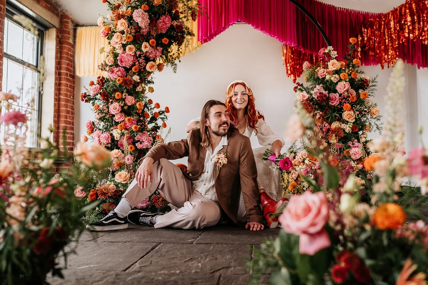 Bride and groom sat amongst colourful flowers in Chapter Hall a Leeds wedding venue