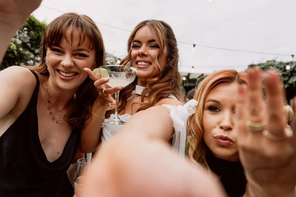 Bride and bridesmaids reaching out for the camera and smiling captured by Steph in her alternative wedding photography style
