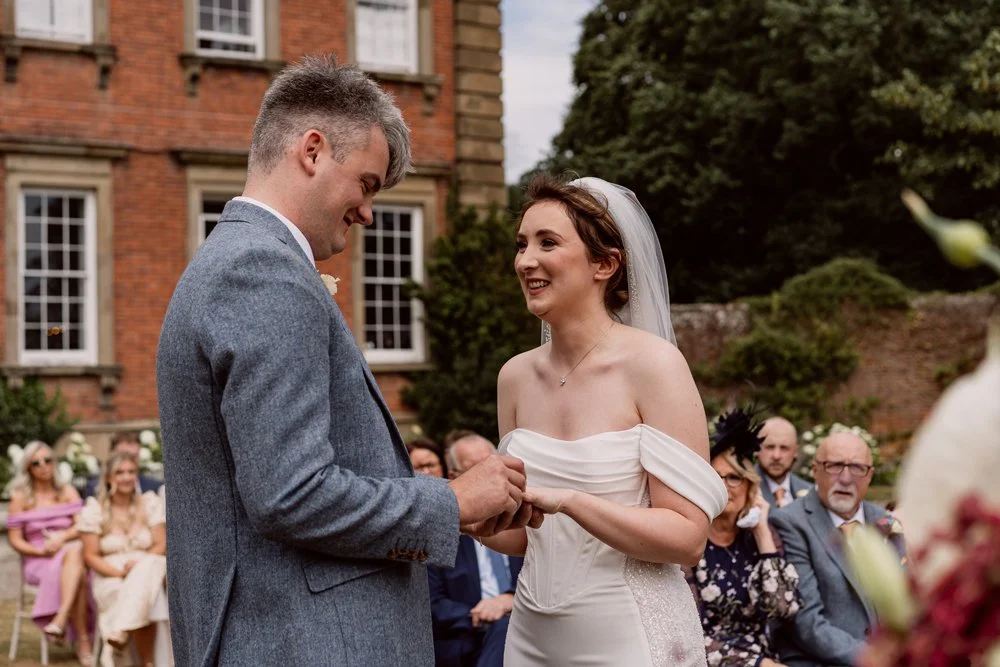 Groom putting wedding ring on brides finger as they smile on their Birmingham wedding day