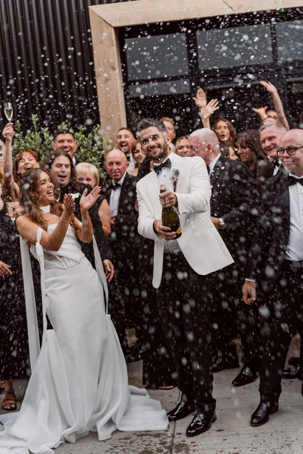 groom popping champagne with guests in the background cheering