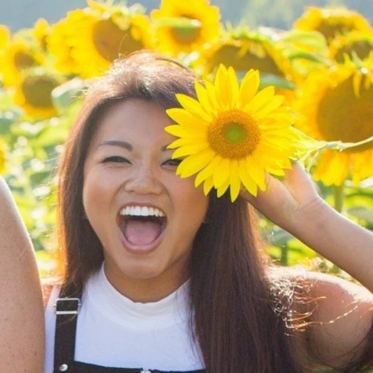 Smiling woman holding a sunflower in a field of sunflowers.