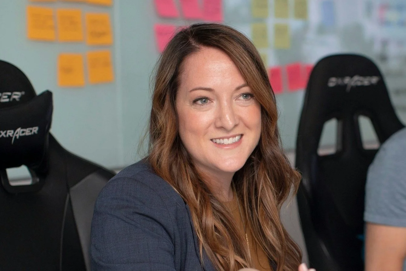 Woman smiling in an office setting with sticky notes in the background.