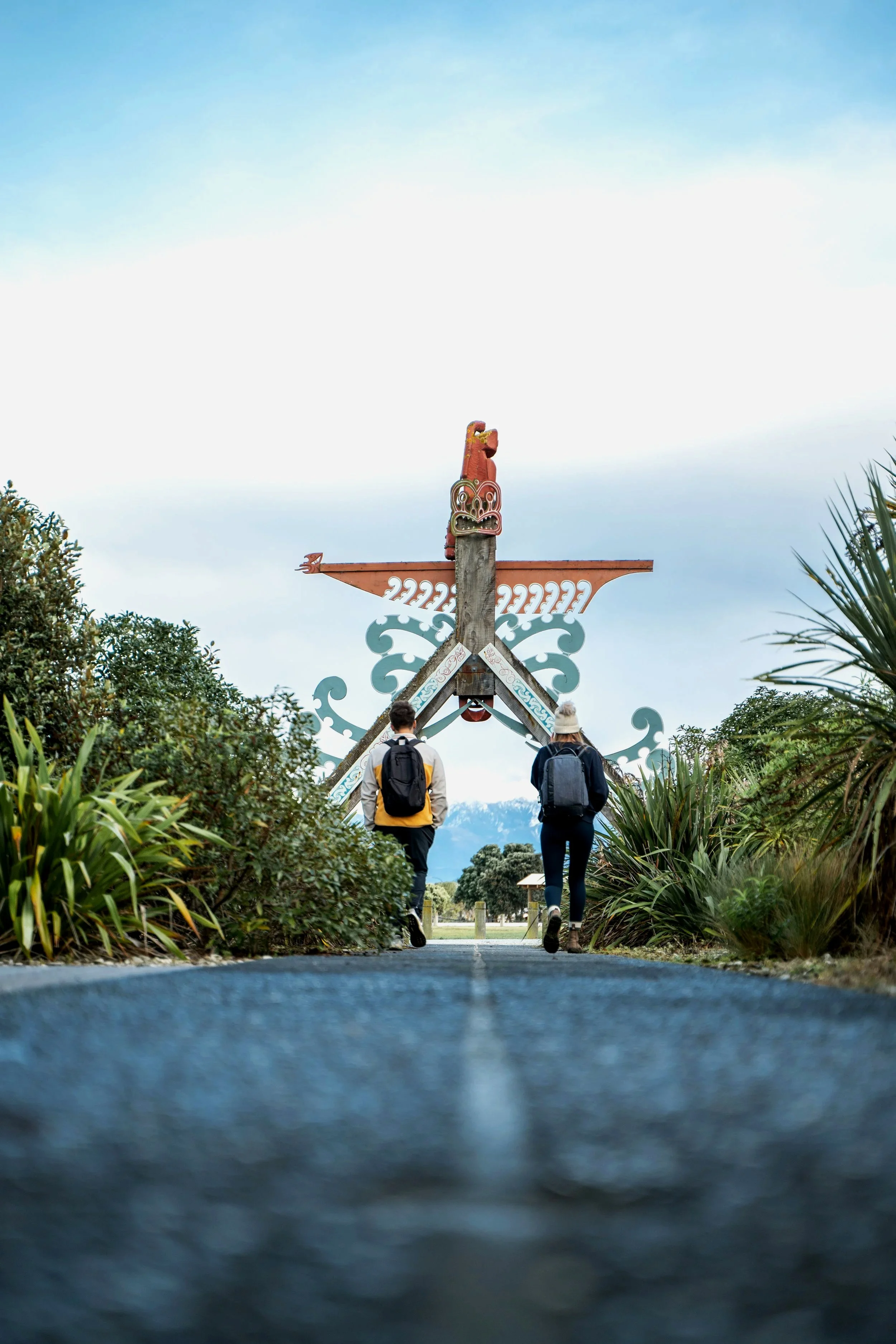 People walking near the entrance to the South Bay walkway, featuring Māori artworks, Kaikōura
