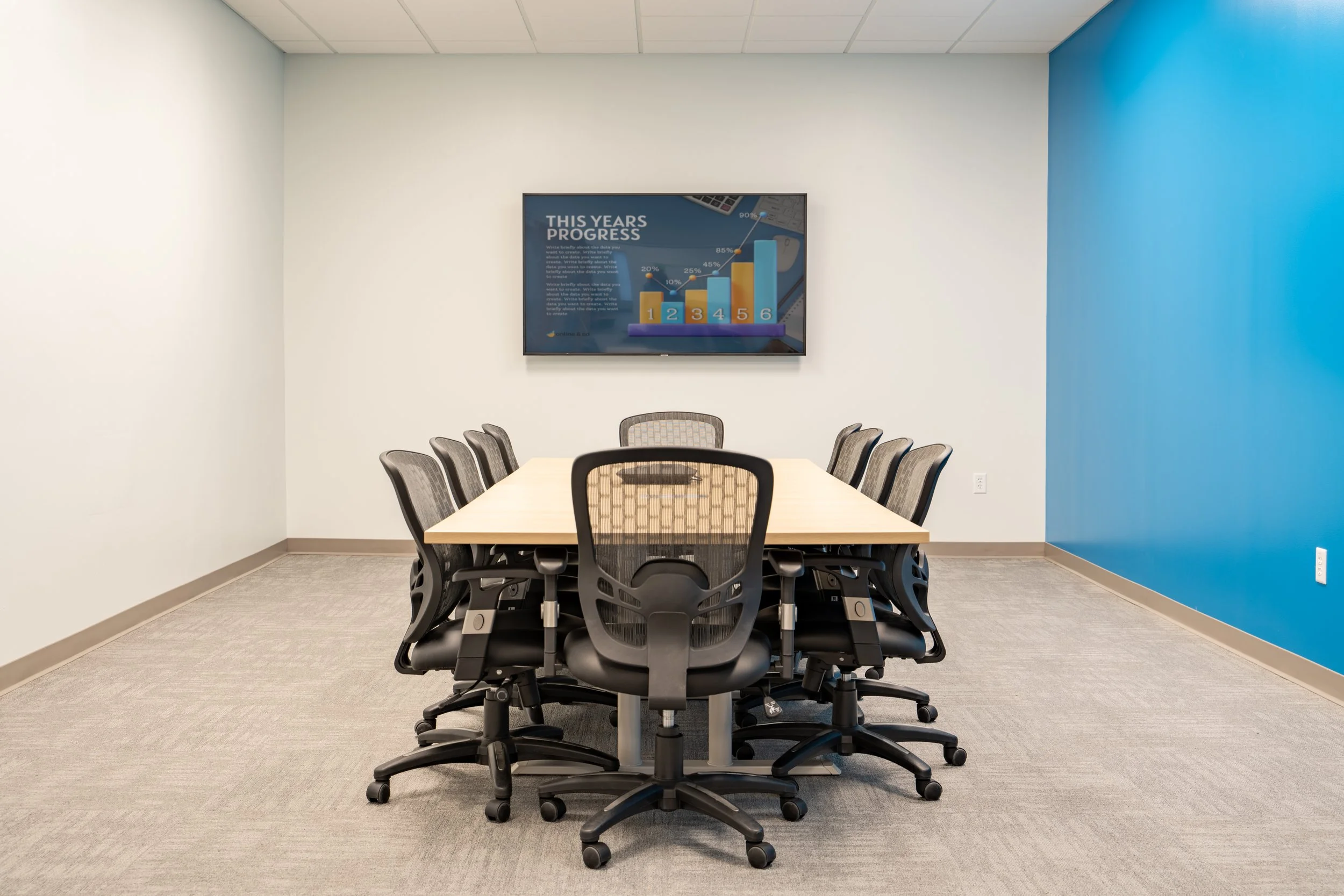 G4CM commercial office construction featuring a modern conference room, blue accent wall, wall-mounted display, and ergonomic seating.