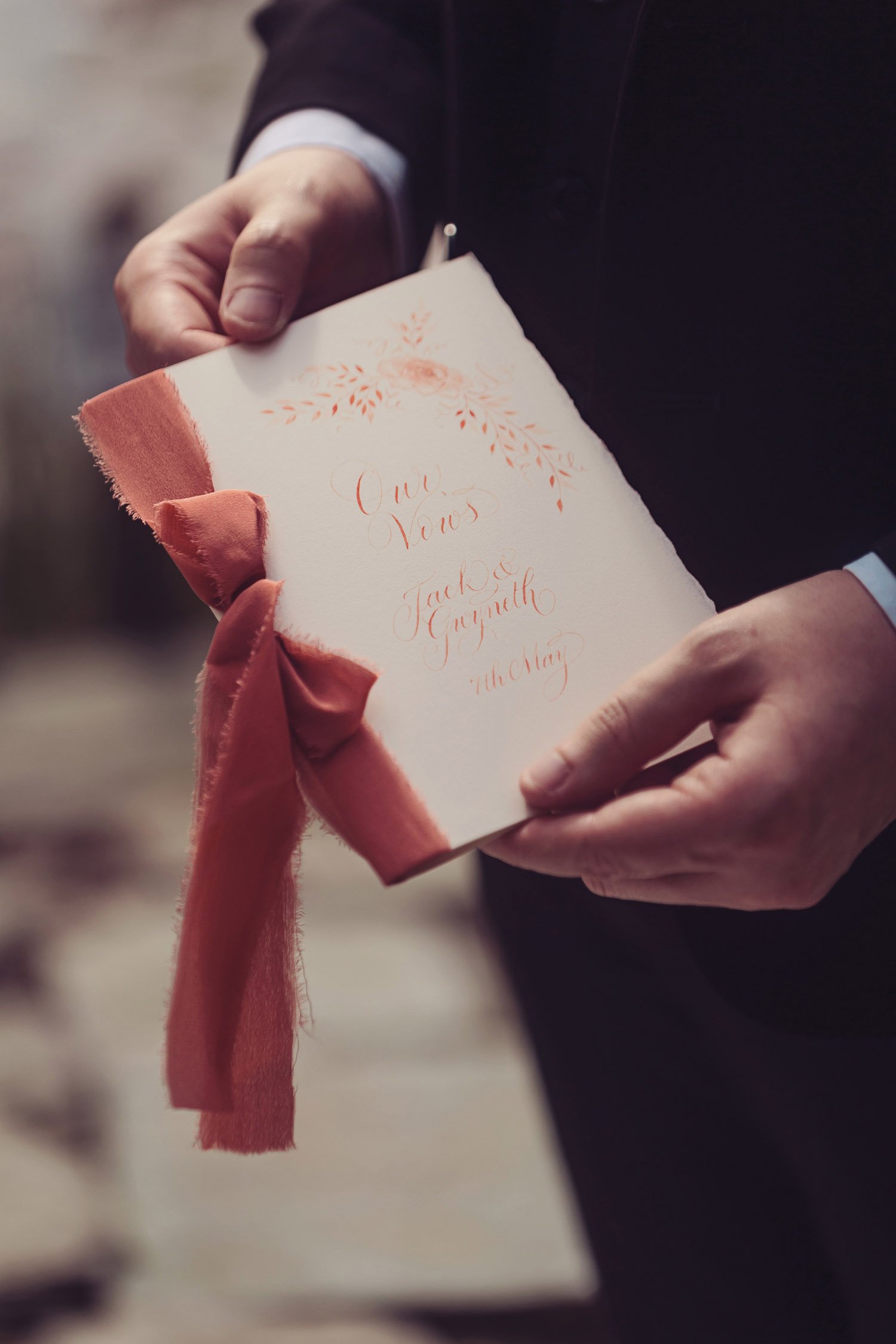 A man holds a wedding vow booklet with a cover in calligraphy