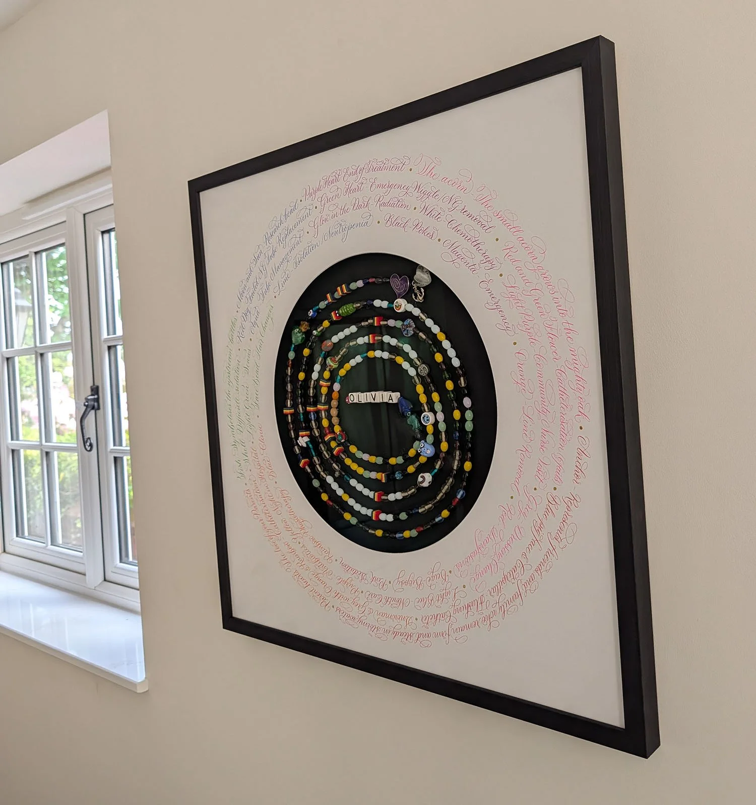 Calligraphy in colourful circles around a string of beads in a picture frame | By Moon & Tide Calligraphy UK