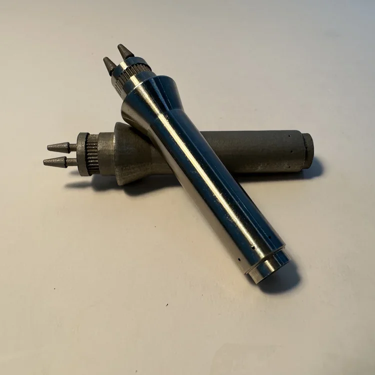 Three soldering iron tips placed on a white surface, with one soldering iron handle visible in the background.