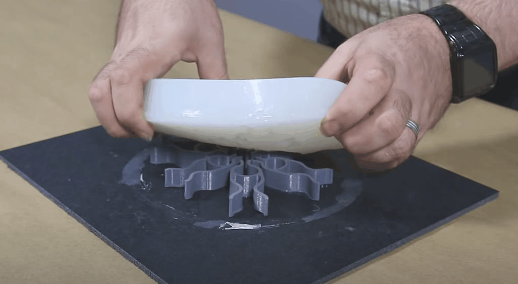 Person wearing a watch and ring holds a white bowl above a silicone mold with a snowflake shape on a black surface.