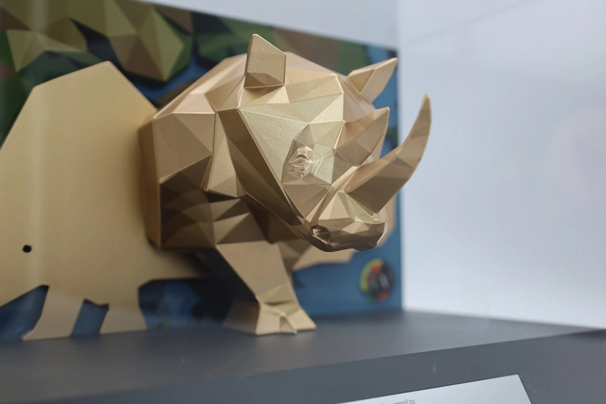 Three quarter view of a 3D printed golden rhino on a black base plate with a metal name plate, encased in an acrylic box