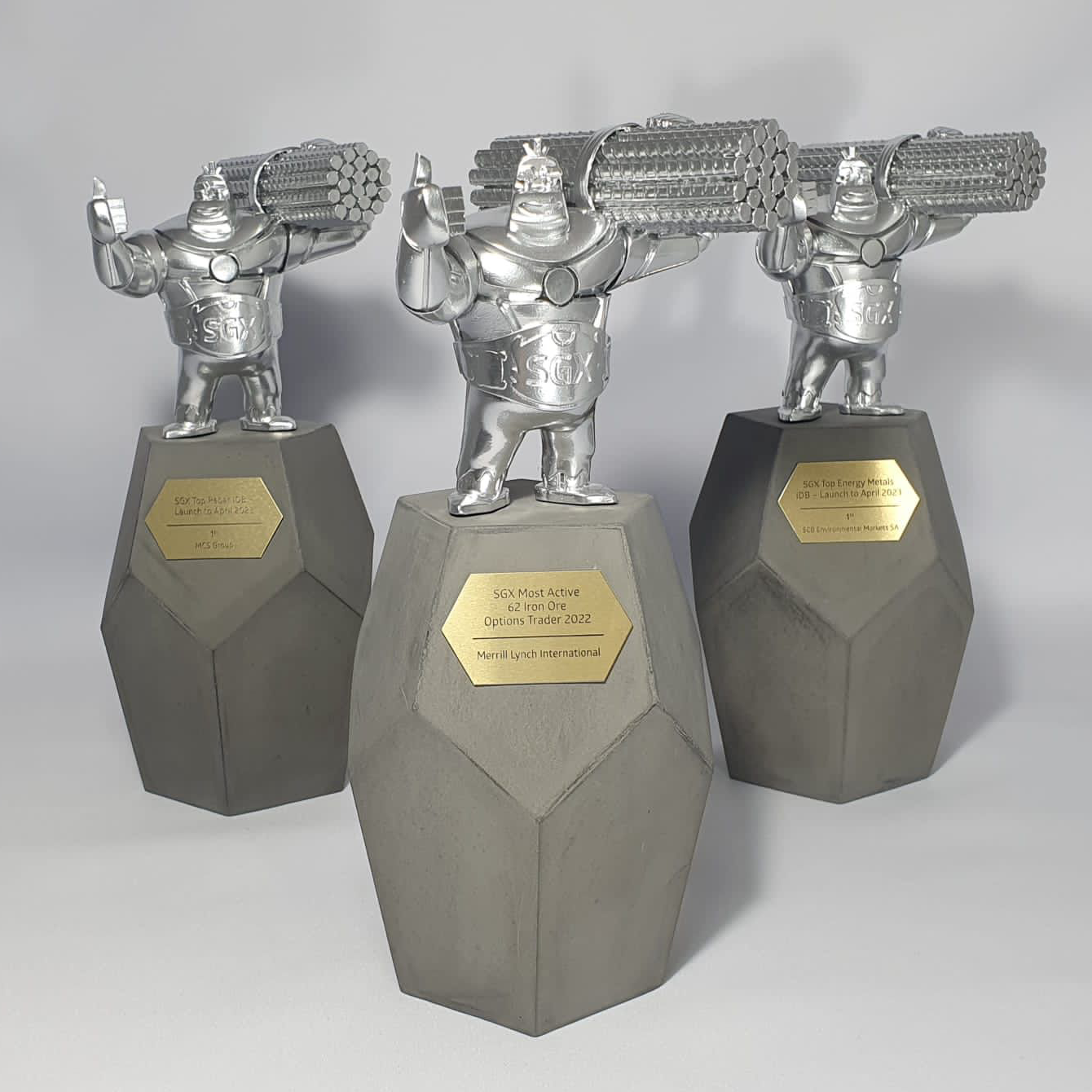 Three metallic trophies with cartoon-style miners lifting pickaxes, mounted on hexagonal gray bases with gold plaques, set against a plain background.