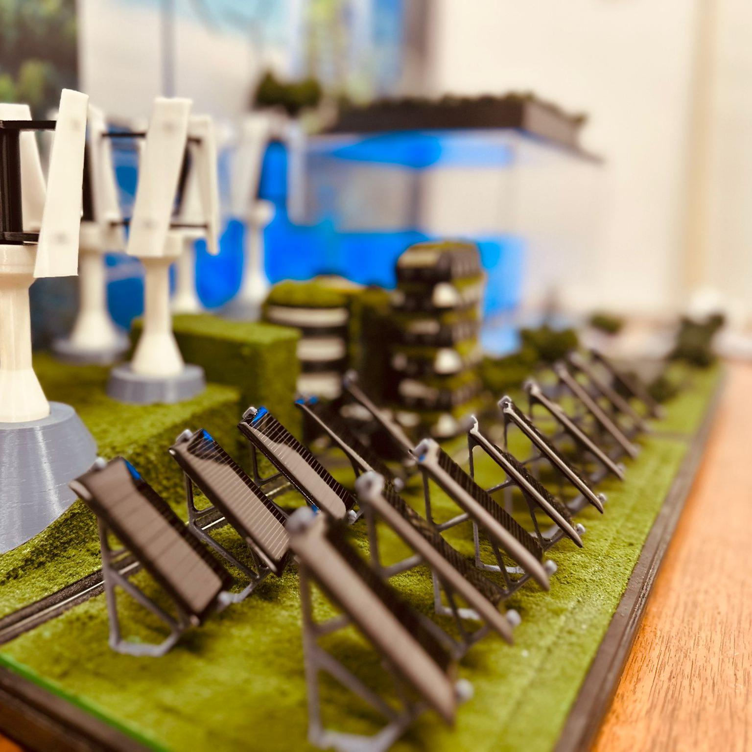 Close-up of miniature model stadium seats and bleachers on a green base, with some white structures and a blue background in the blurred background.
