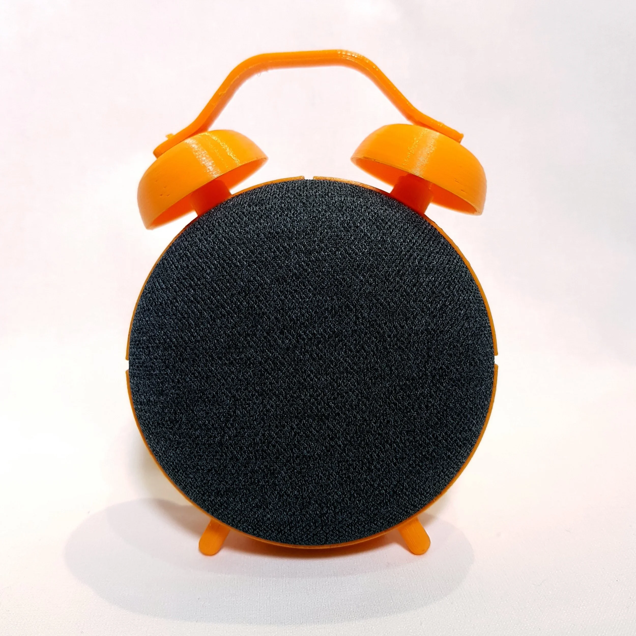 Orange and black portable speaker designed to resemble a vintage alarm clock, with two orange bells on top and small orange feet at the bottom.