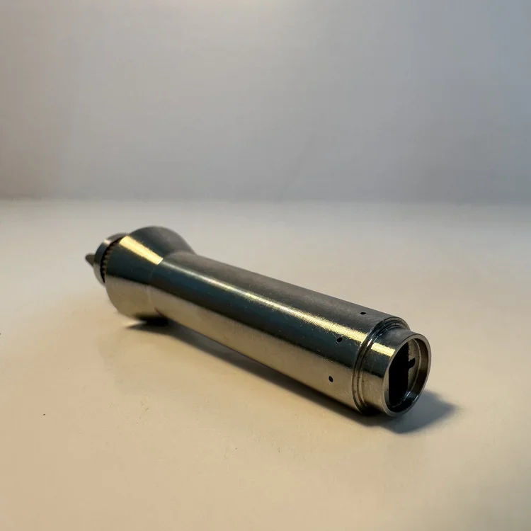 A metal cylindrical tool with a tapered end and small holes along its body, resting on a white surface.