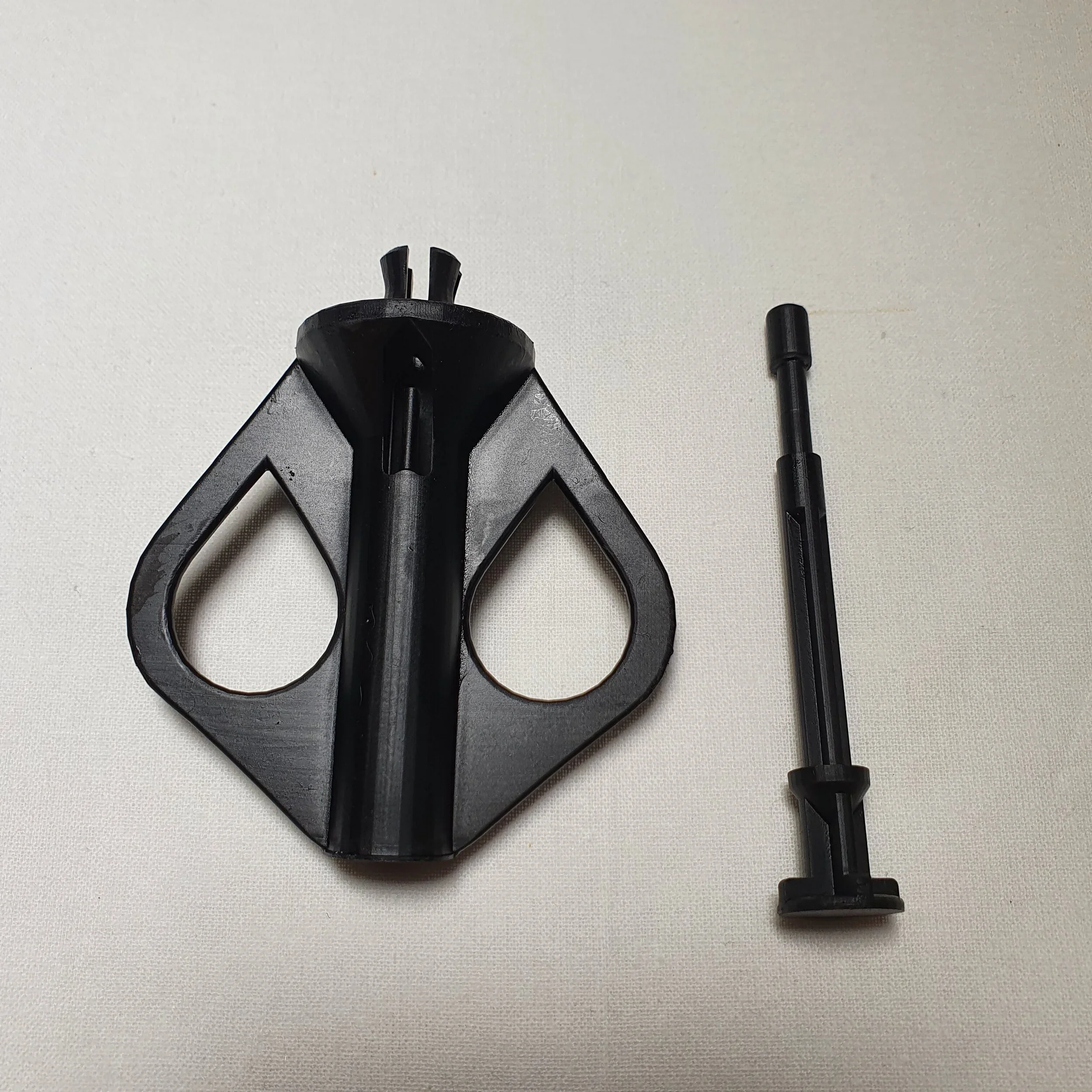 Plastic tool with two large teardrop-shaped openings and a long black rod with a cylindrical end, laid on a white surface.