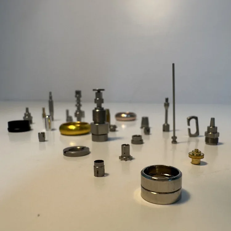 Various small metallic components arranged on a white surface, with a plain light background.