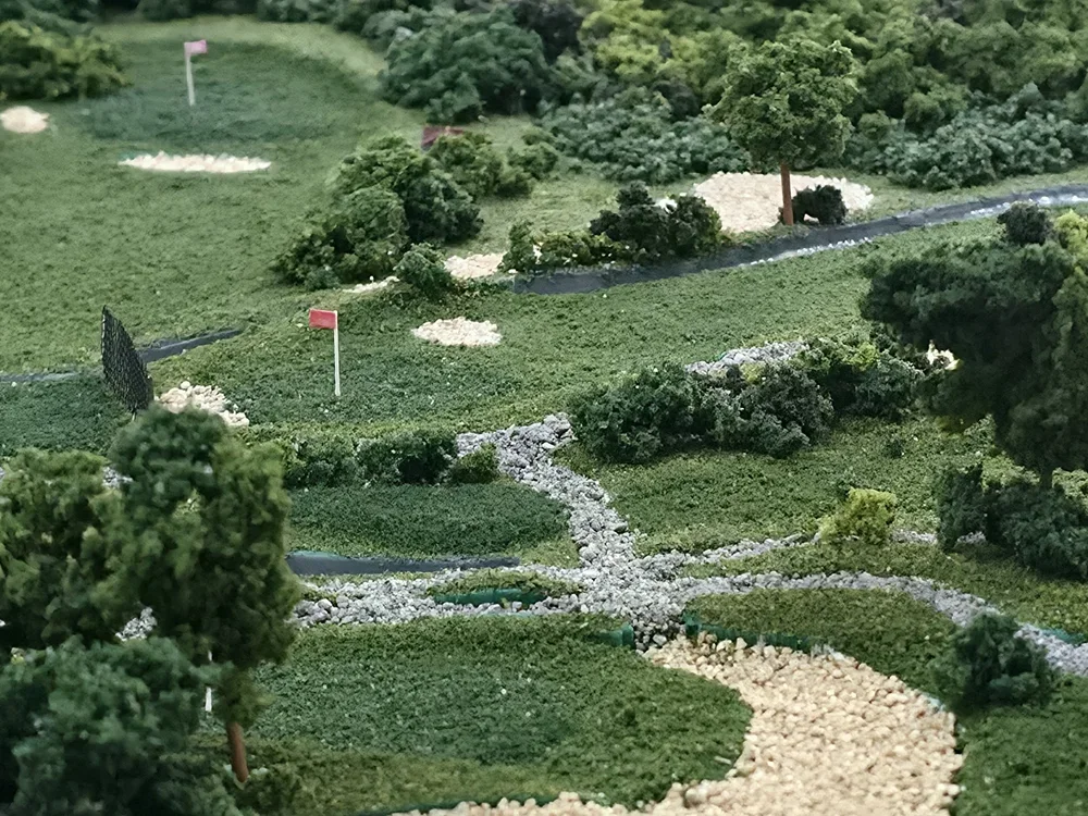 A miniature landscape model of a golf course with small trees, bushes, and pathways.