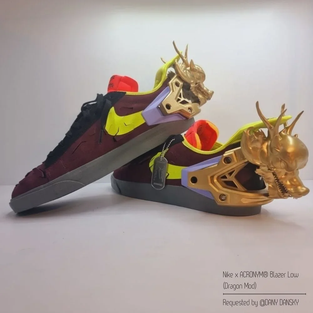 A pair of Nike x ACRONYM Blazer Low Dragon Mod sneakers with metallic gold dragon head details on the heels, black, maroon, neon yellow, and lavender accents, displayed side by side against a plain background.